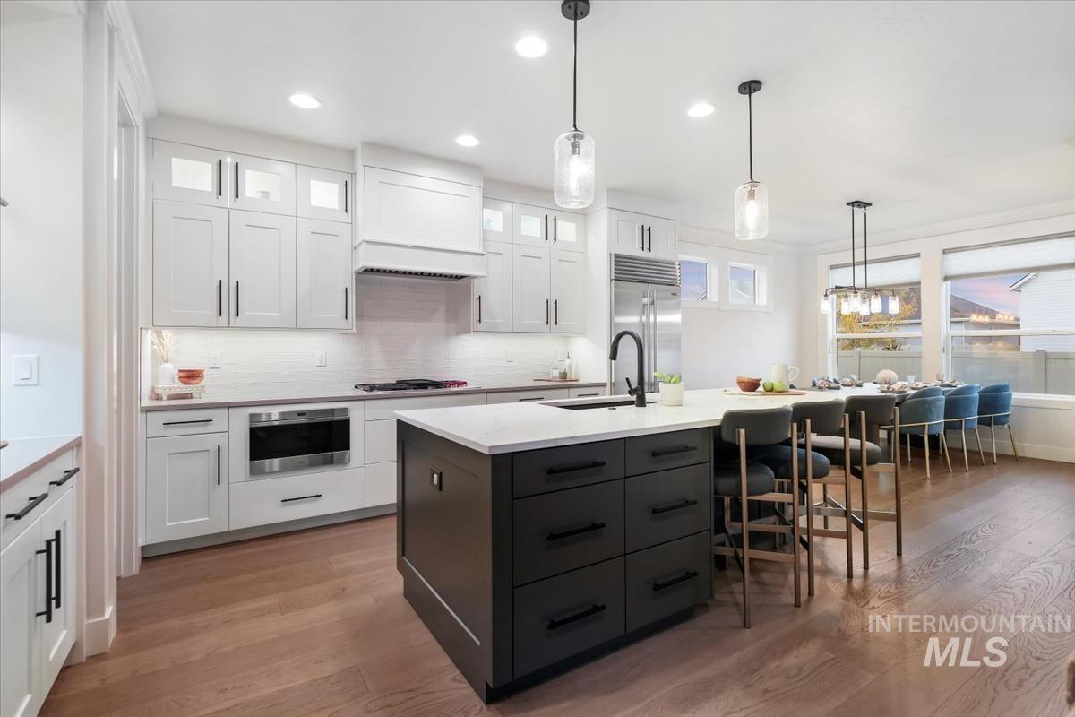 Kitchen with white cabinetry, pendant lighting, glass insert cabinets, light wood finished floors, and backsplash
