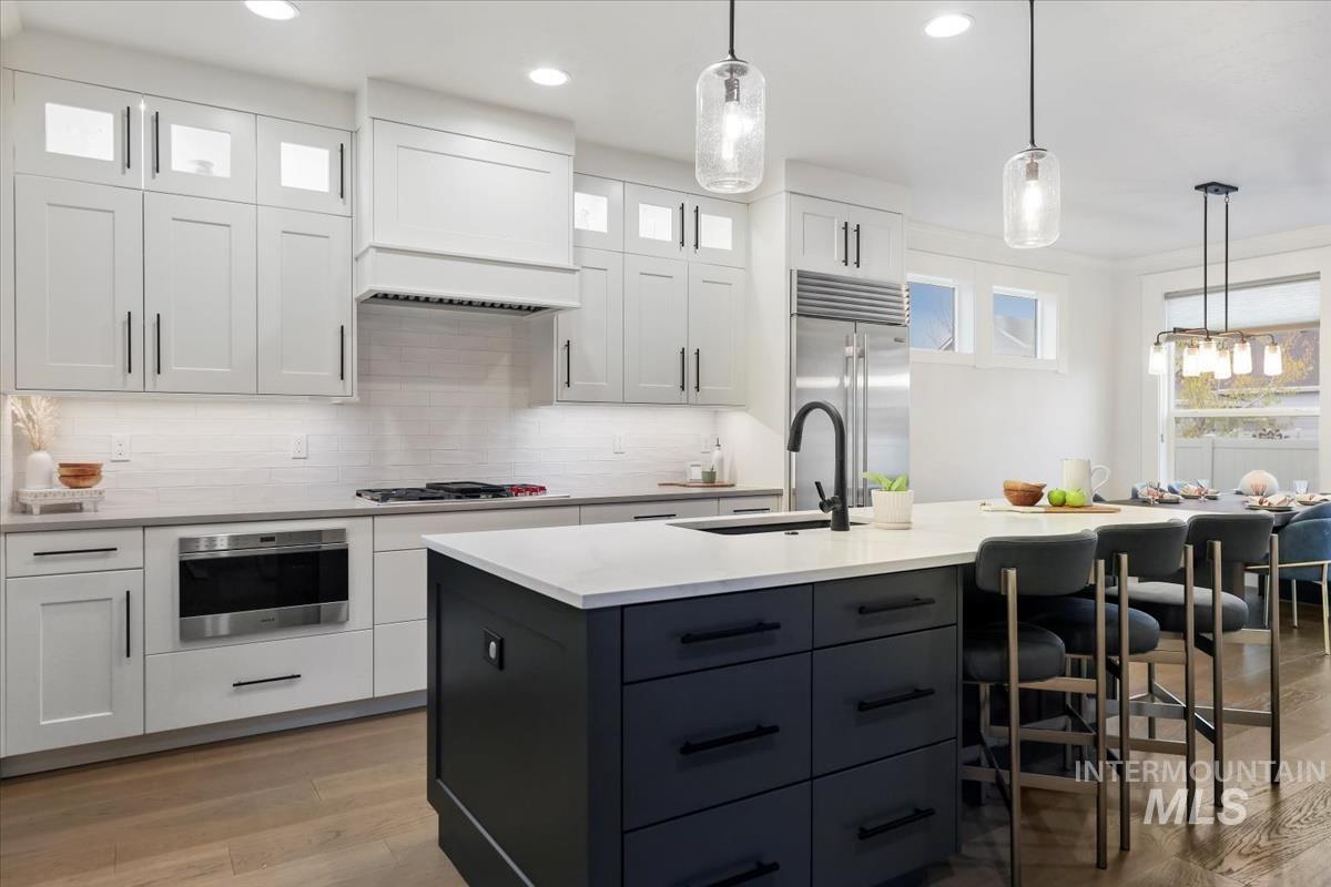 Kitchen with decorative light fixtures, white cabinets, glass insert cabinets, a center island with sink, and recessed lighting