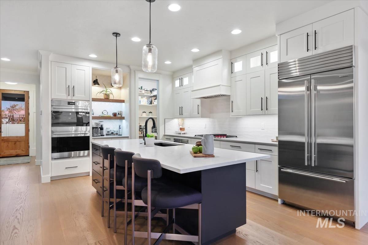 Kitchen with white cabinetry, appliances with stainless steel finishes, backsplash, a kitchen island with sink, and pendant lighting