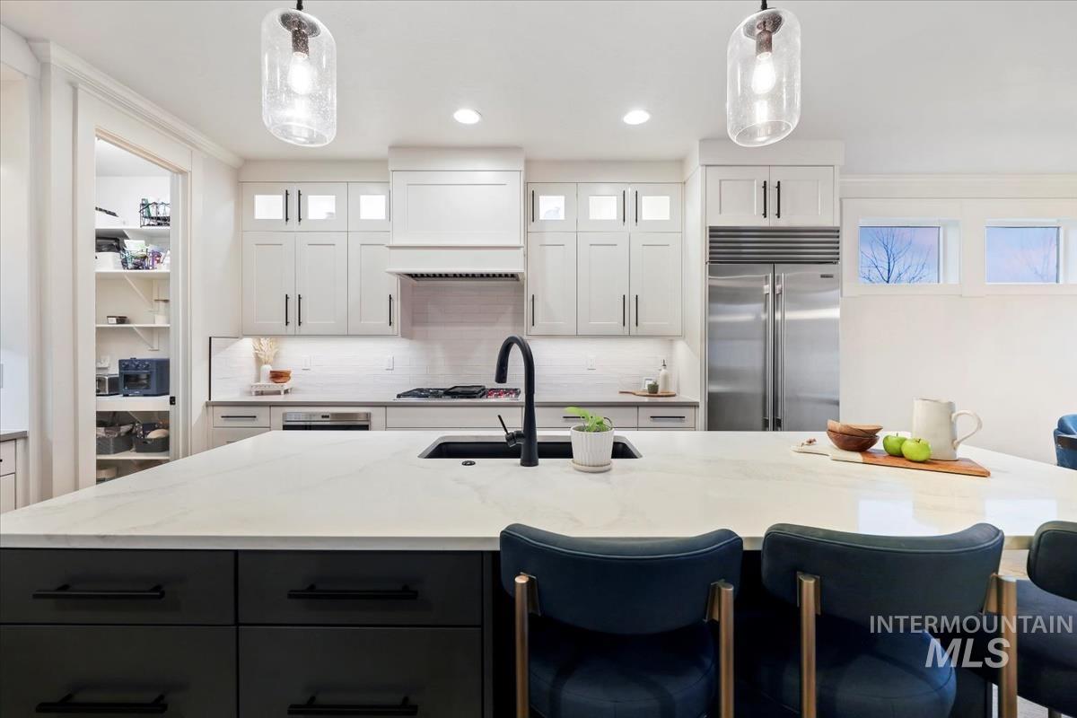 Kitchen featuring decorative backsplash, white cabinets, built in refrigerator, light stone countertops, and recessed lighting