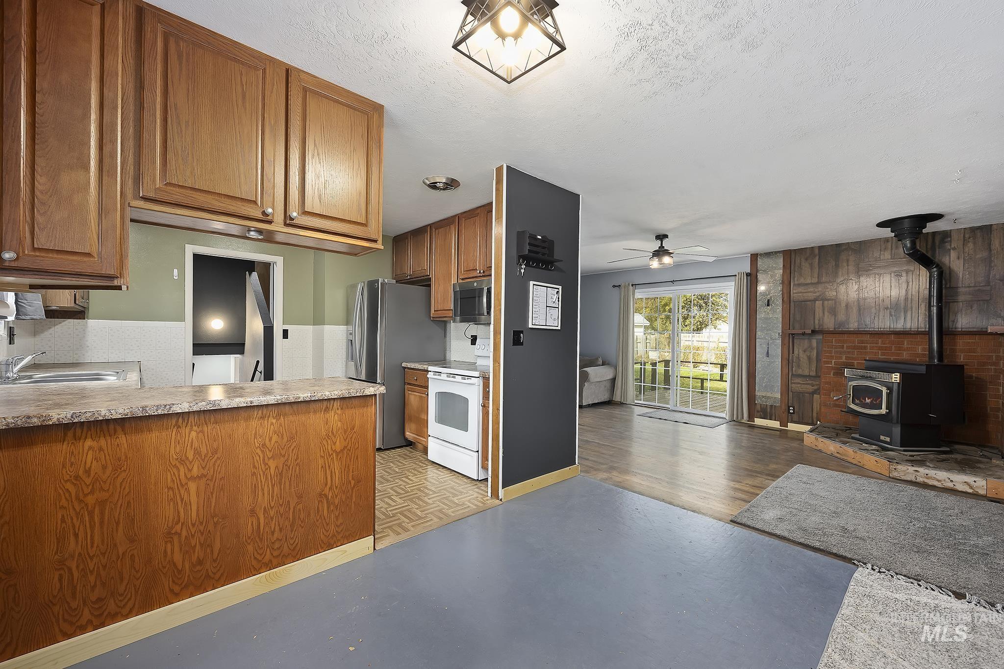 Kitchen featuring brown cabinets, a wood stove, a textured ceiling, stainless steel appliances, and open floor plan