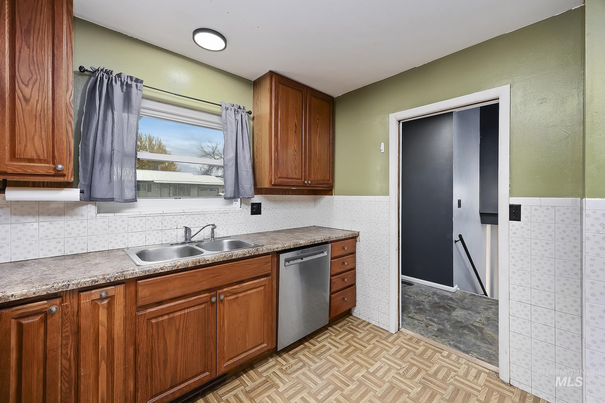 Kitchen featuring brown cabinets, dishwasher, and a wainscoted wall