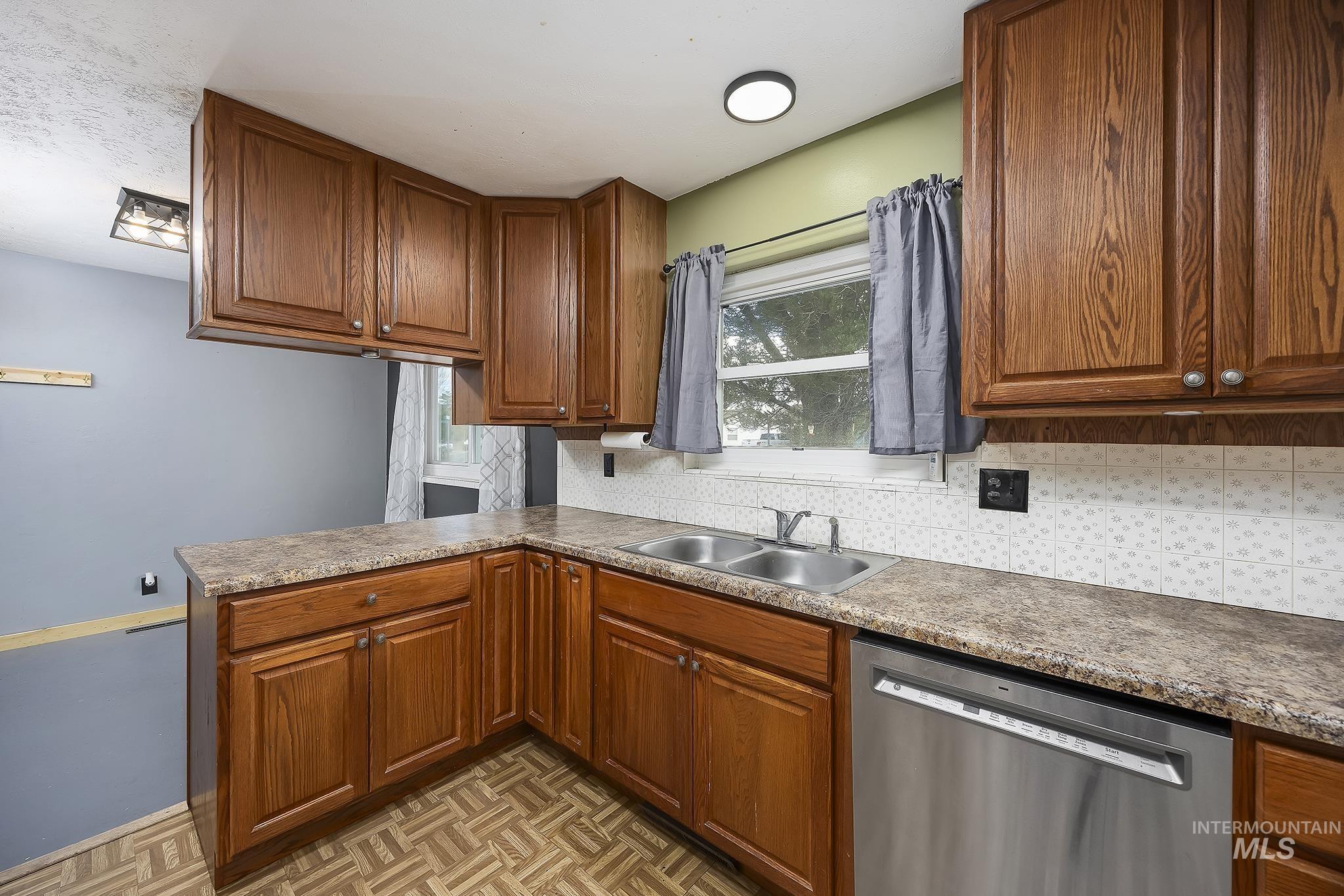Kitchen with dishwasher, decorative backsplash, a peninsula, and brown cabinetry