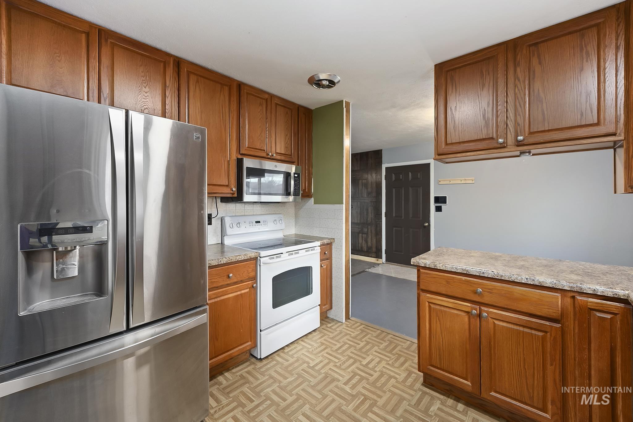 Kitchen with appliances with stainless steel finishes, brown cabinets, light countertops, and decorative backsplash