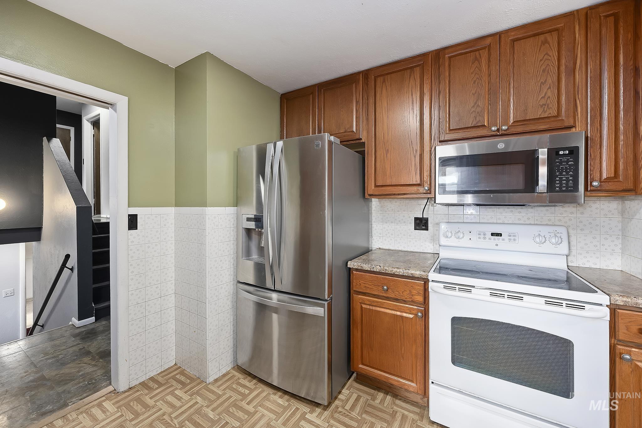 Kitchen featuring stainless steel appliances, brown cabinetry, tile walls, and a wainscoted wall