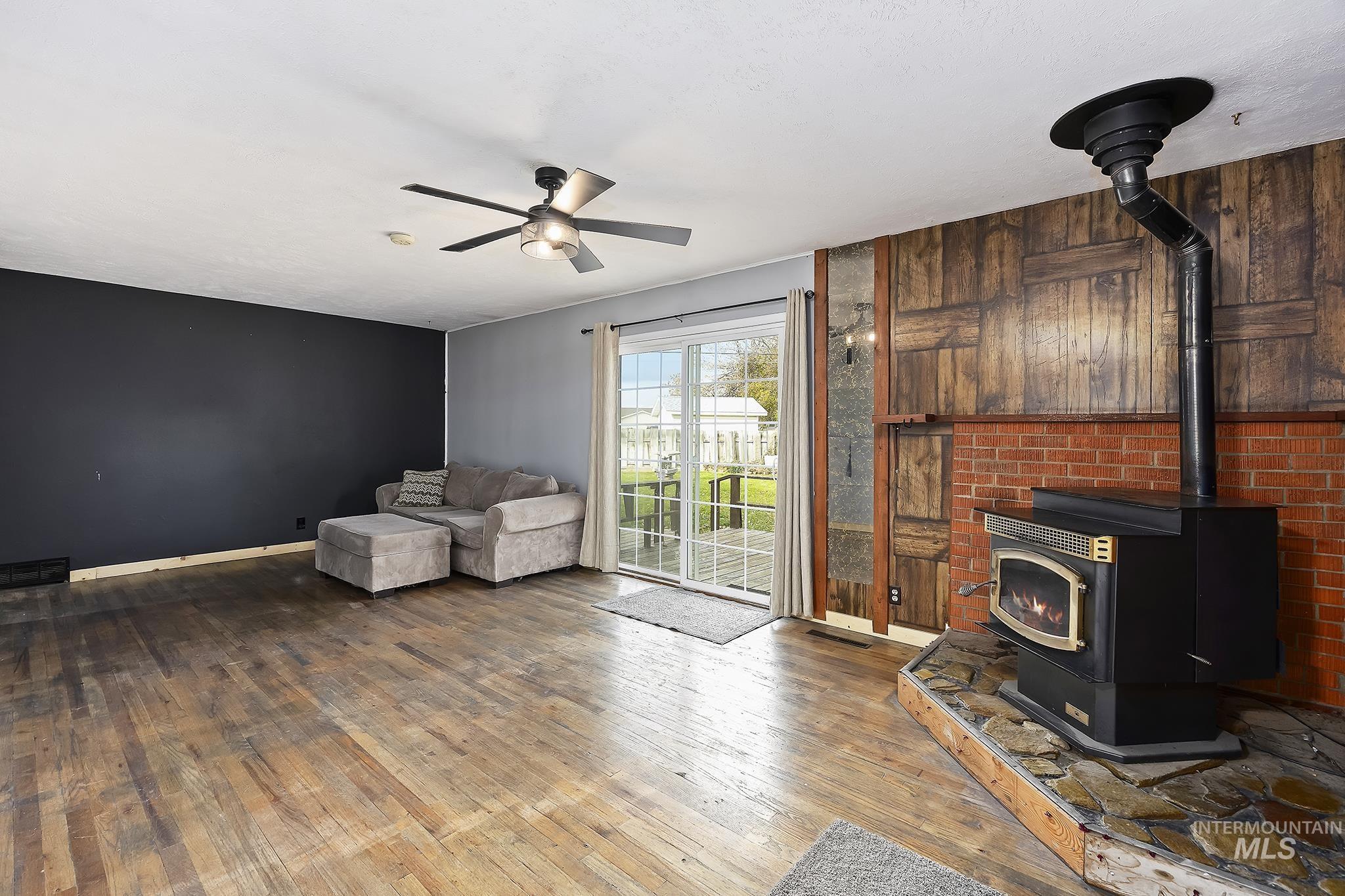 Living area with a wood stove, hardwood / wood-style flooring, and ceiling fan