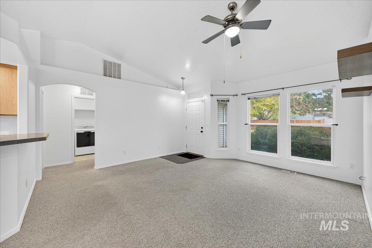 Unfurnished living room featuring light colored carpet, ceiling fan, high vaulted ceiling, arched walkways, and washer / dryer
