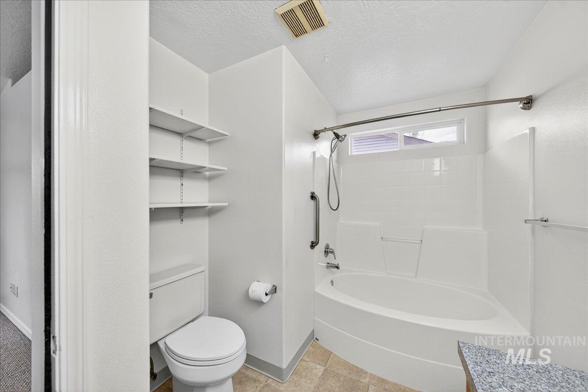 Bathroom featuring a textured ceiling, bathing tub / shower combination, and light tile patterned flooring