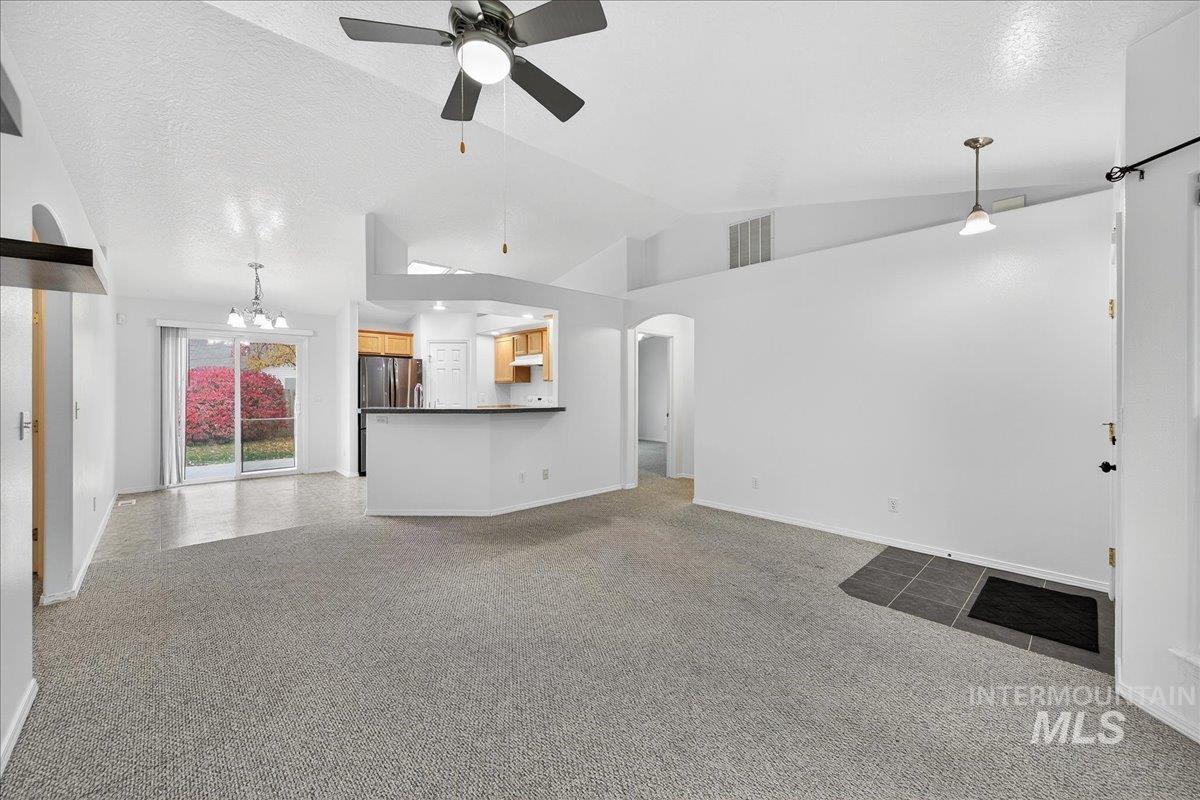 Unfurnished living room featuring arched walkways, ceiling fan, light colored carpet, a textured ceiling, and vaulted ceiling