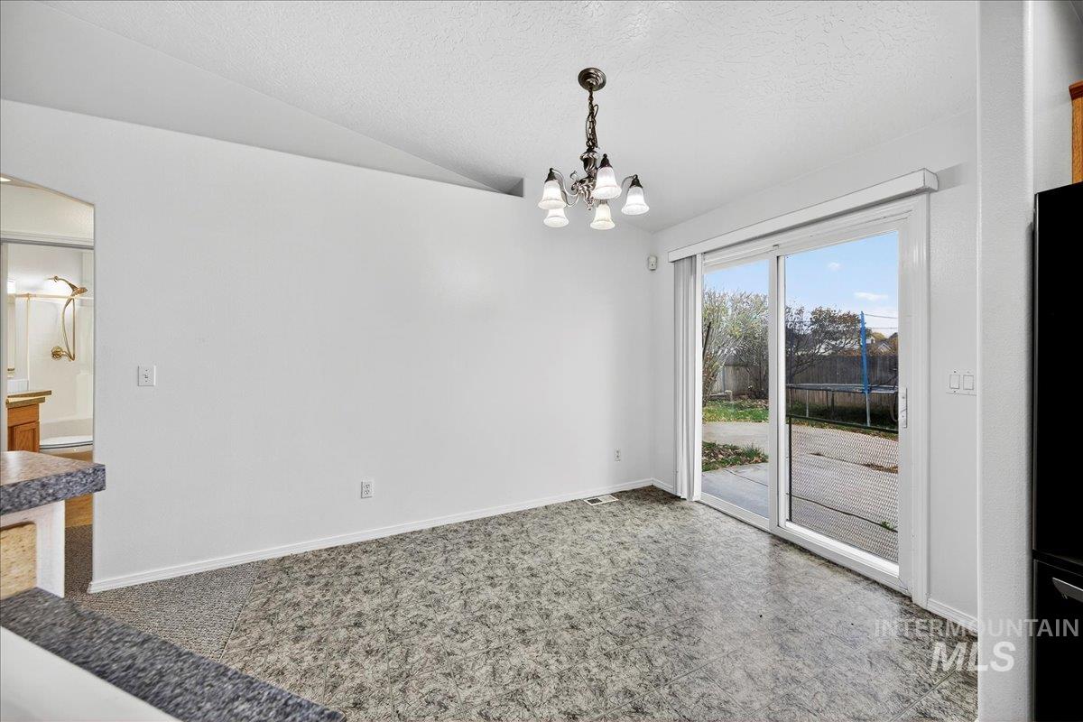 Unfurnished dining area with vaulted ceiling, a textured ceiling, and a chandelier