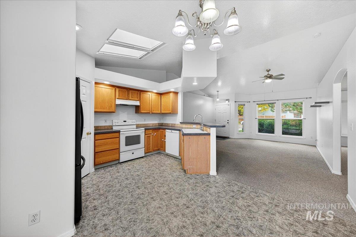 Kitchen with dark countertops, hanging light fixtures, a peninsula, white appliances, and open floor plan