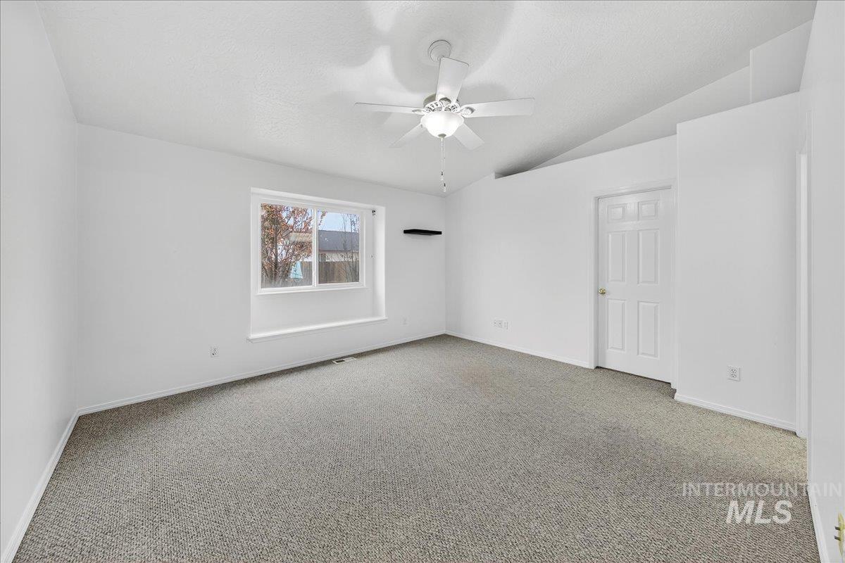 Empty room featuring carpet flooring, vaulted ceiling, ceiling fan, and a textured ceiling