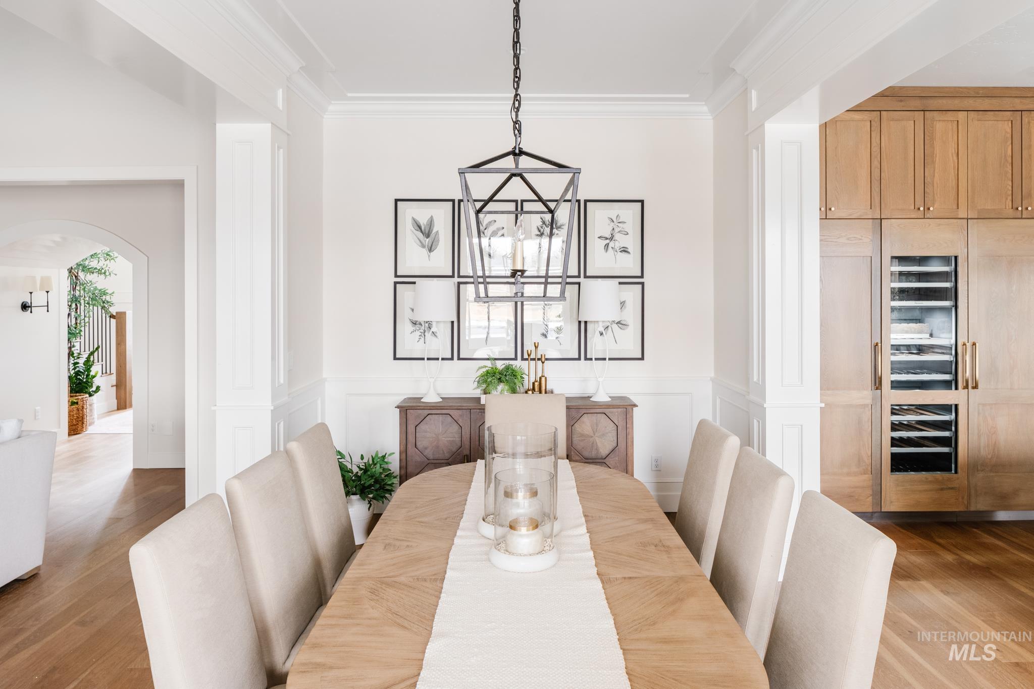 Dining area featuring arched walkways, wood finished floors, ornamental molding, a decorative wall, and a wainscoted wall