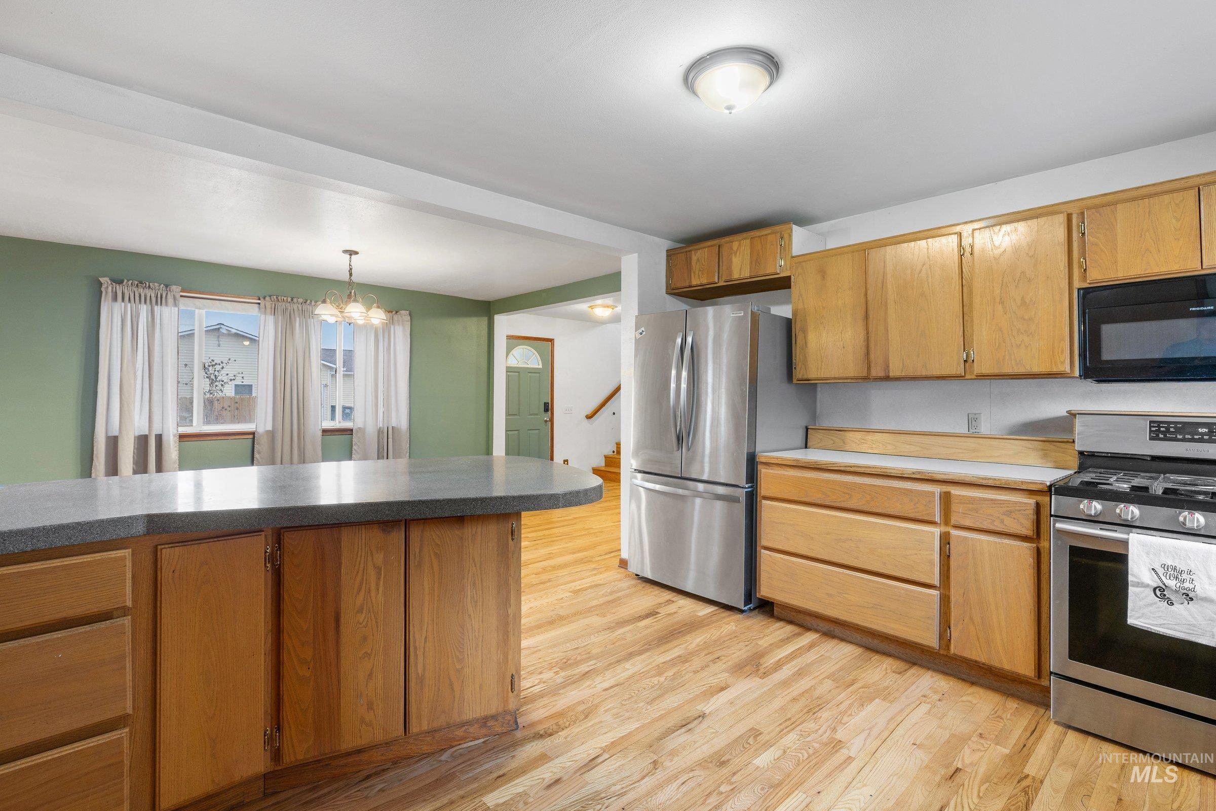 Kitchen featuring appliances with stainless steel finishes, light wood-style flooring, brown cabinetry, a chandelier, and pendant lighting