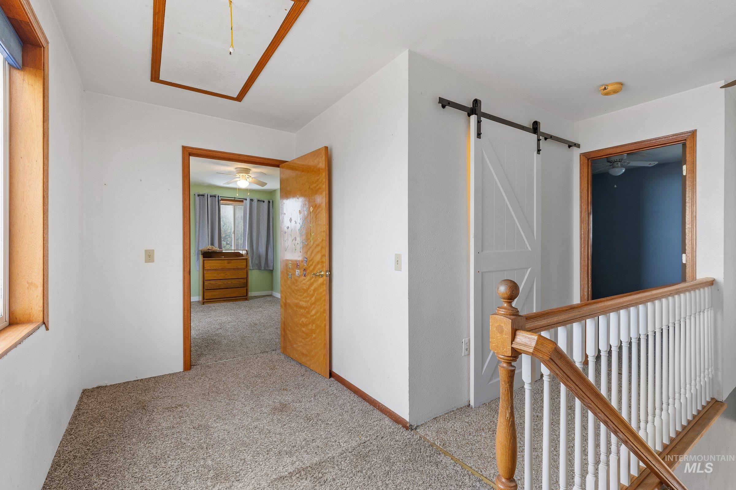 Corridor featuring attic access, light colored carpet, and a barn door