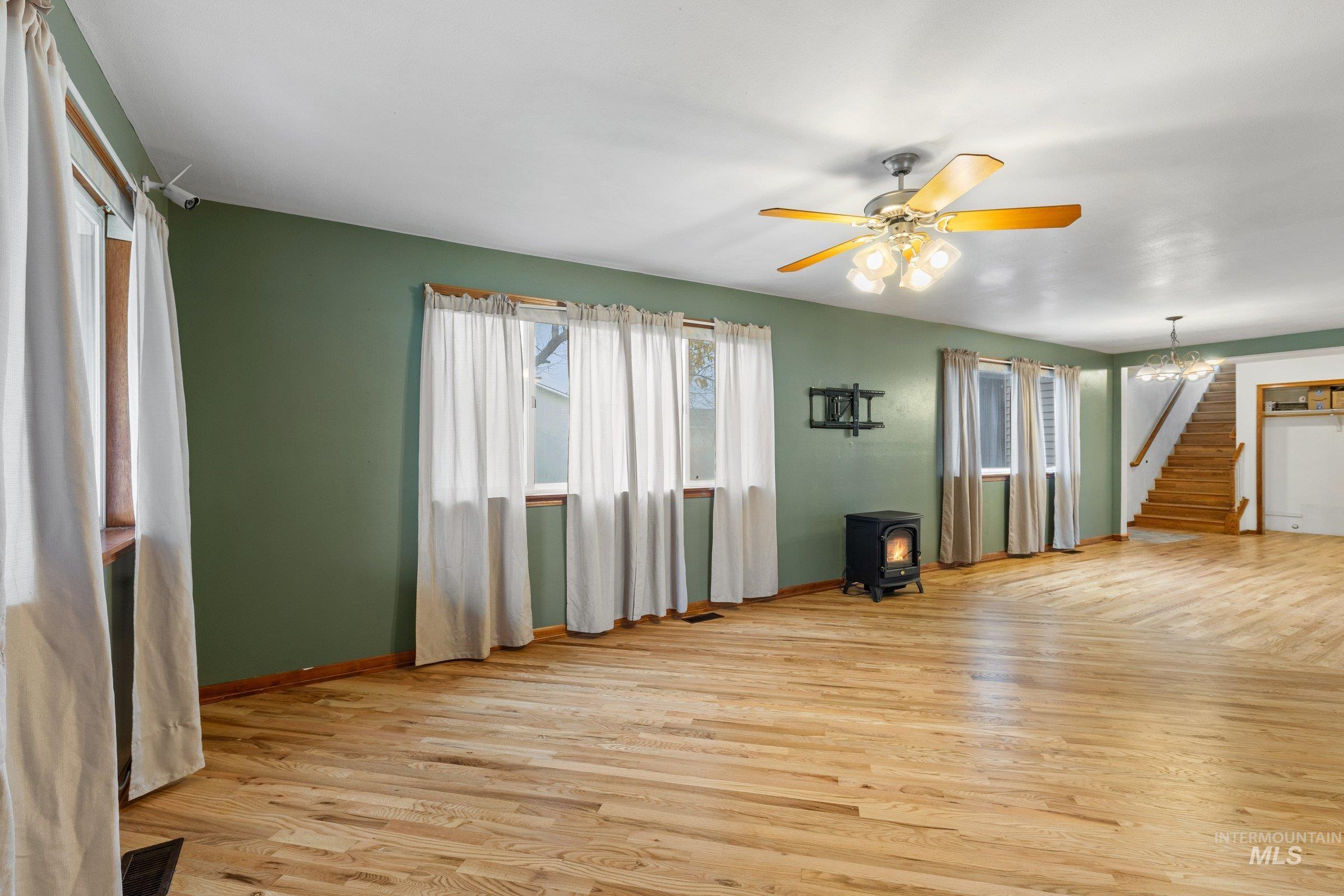Unfurnished living room with light wood-type flooring, a wood stove, stairs, ceiling fan, and a chandelier