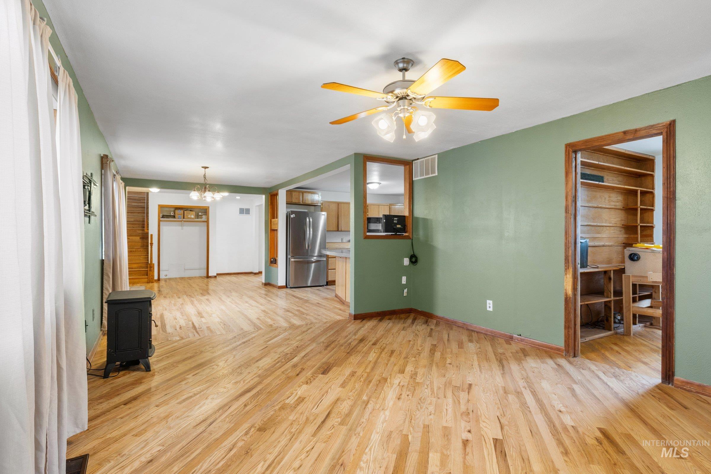 Unfurnished living room featuring light wood finished floors, a chandelier, a wood stove, and a ceiling fan