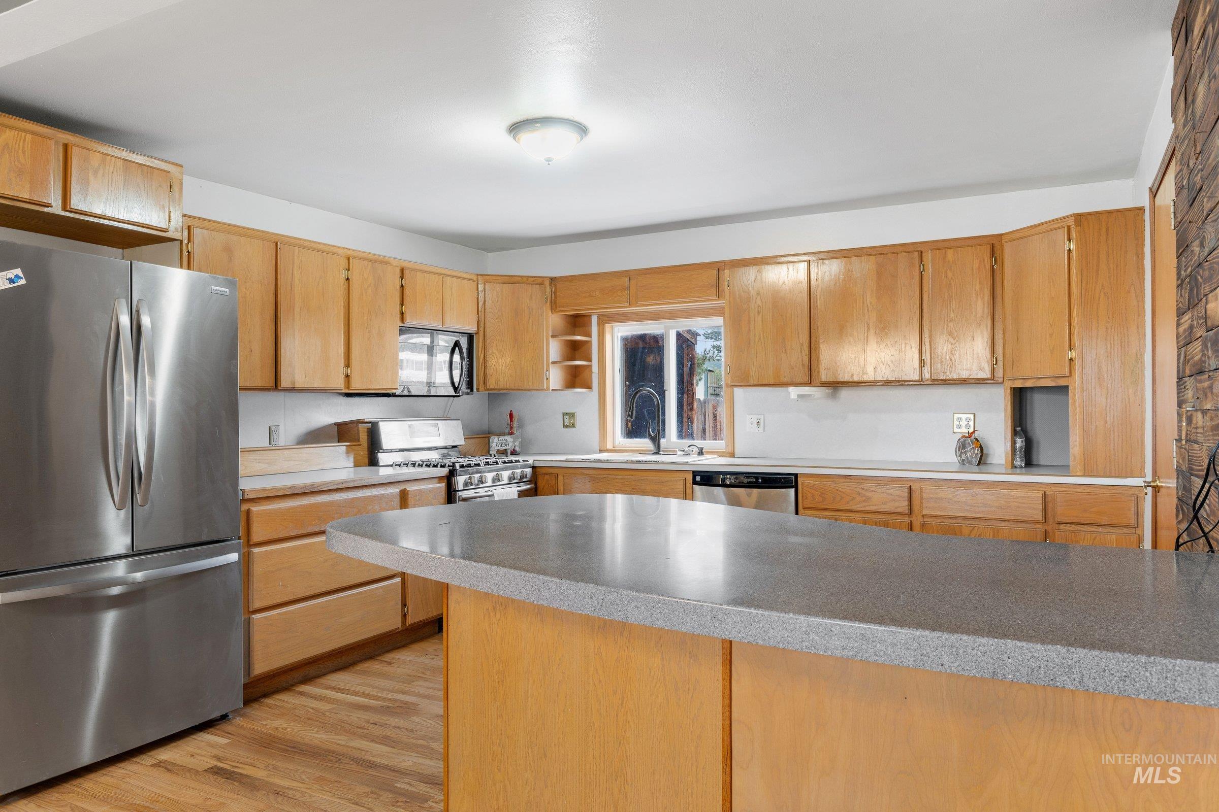 Kitchen featuring appliances with stainless steel finishes, light wood-style floors, light countertops, and open shelves