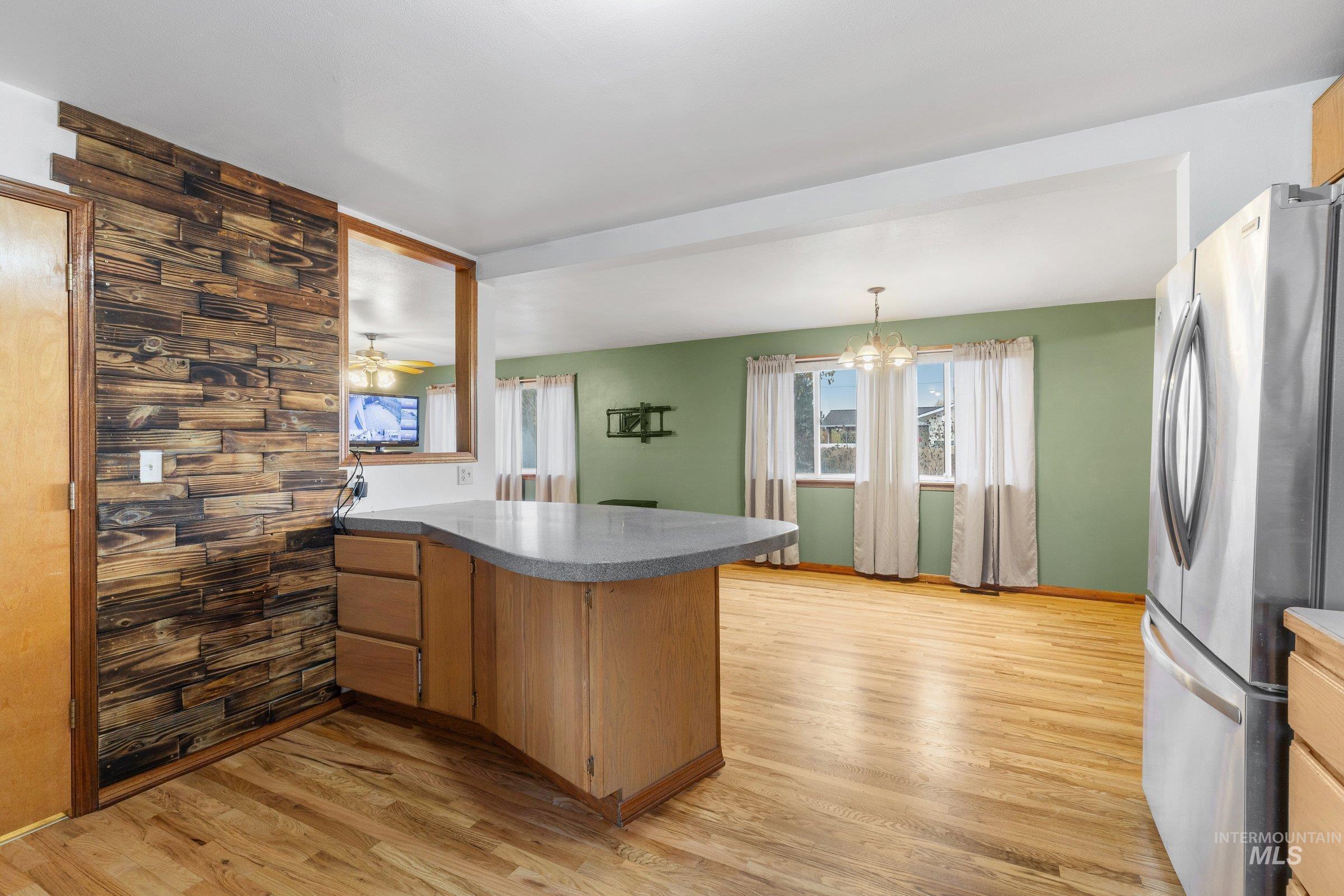 Kitchen featuring a peninsula, freestanding refrigerator, light wood-style floors, a chandelier, and ceiling fan