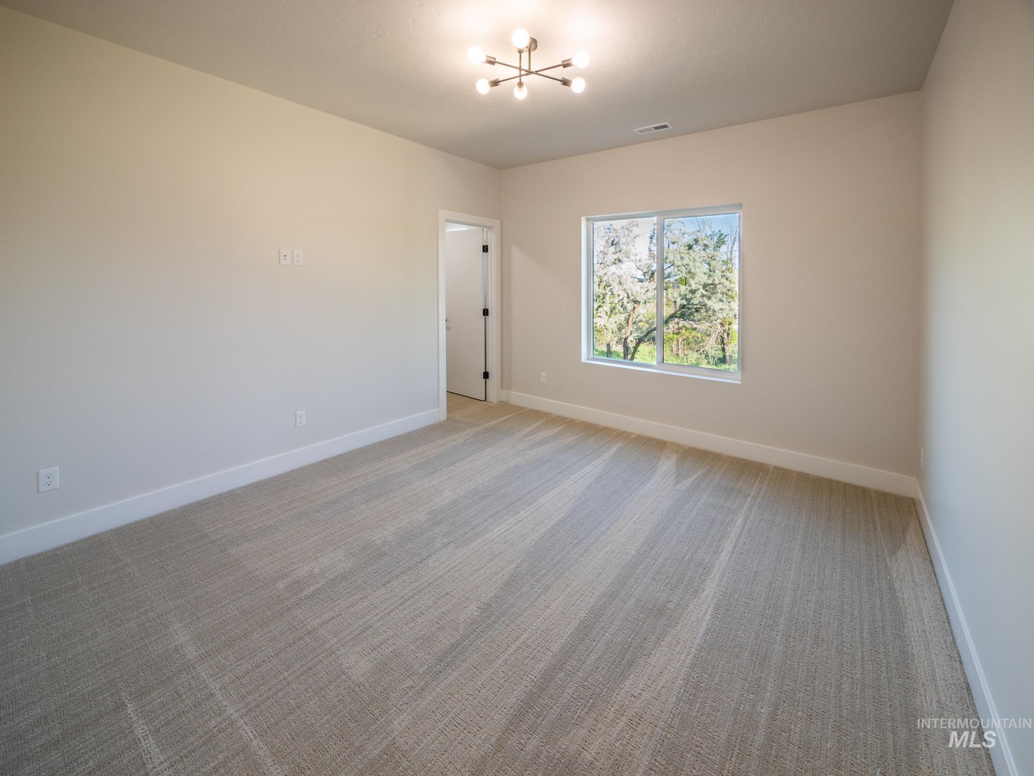 Empty room featuring light carpet and a chandelier