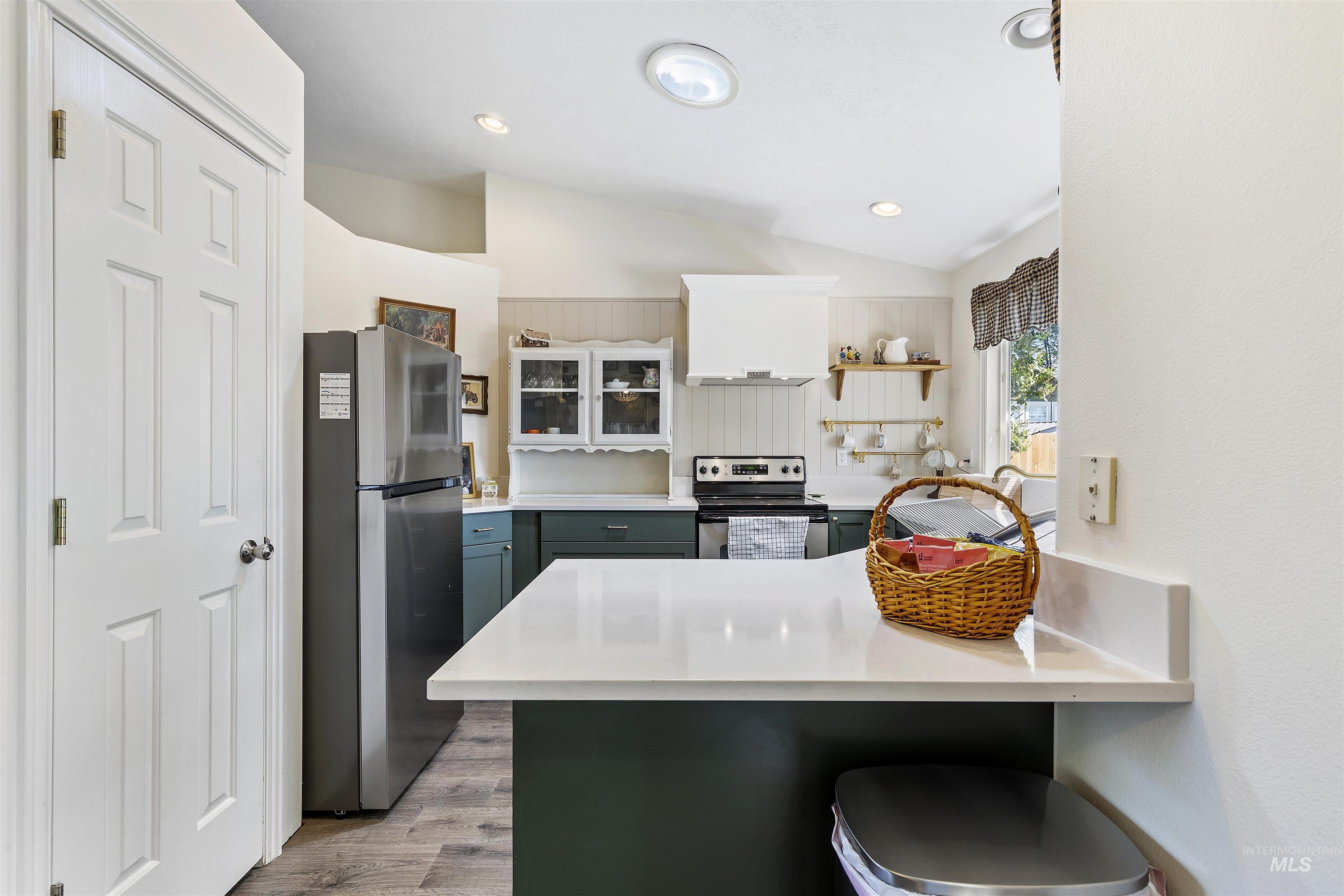 Kitchen featuring a peninsula, stainless steel appliances, a kitchen breakfast bar, vaulted ceiling, and light wood finished floors