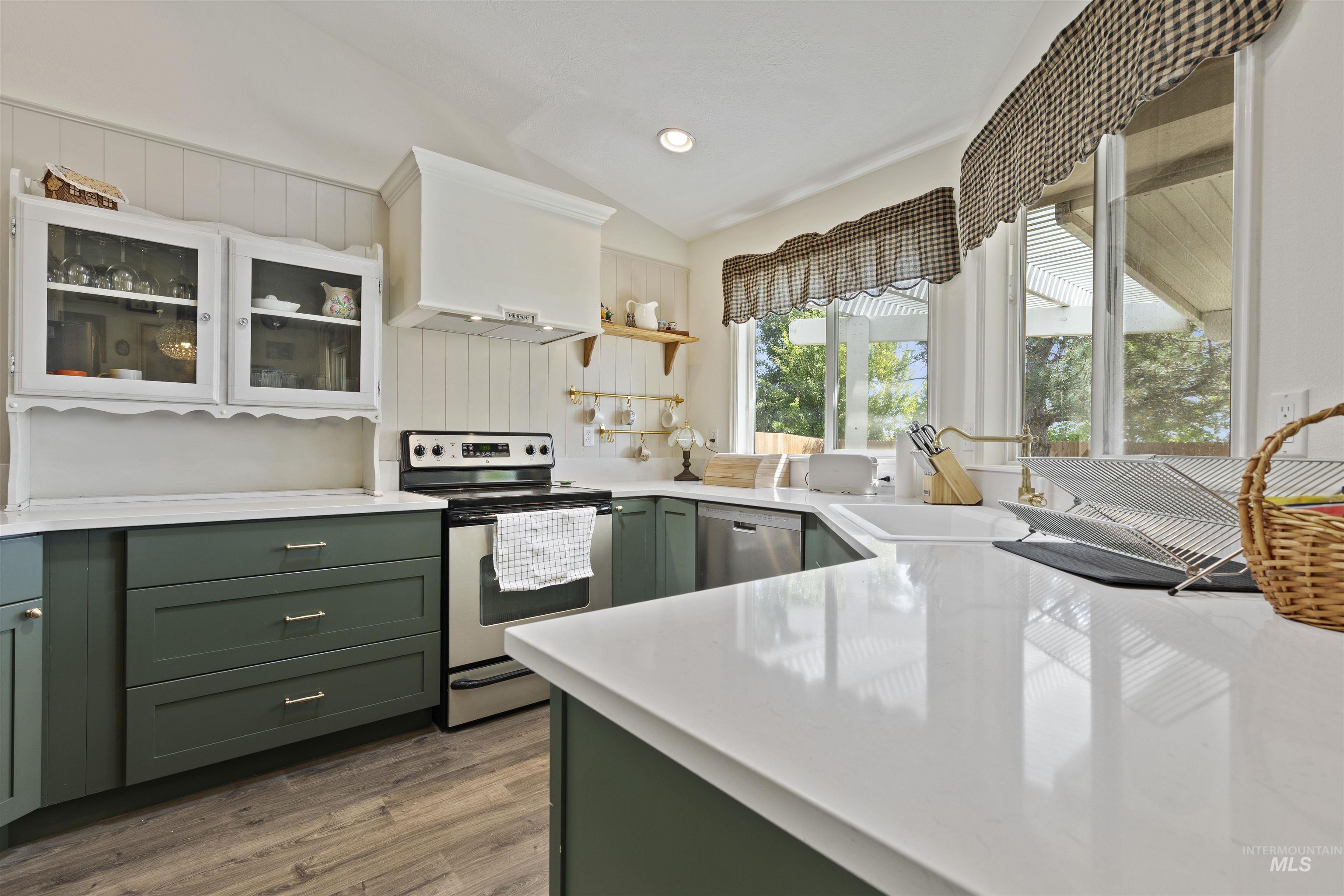 Kitchen featuring green cabinets, stainless steel appliances, dark wood finished floors, wall chimney range hood, and vaulted ceiling