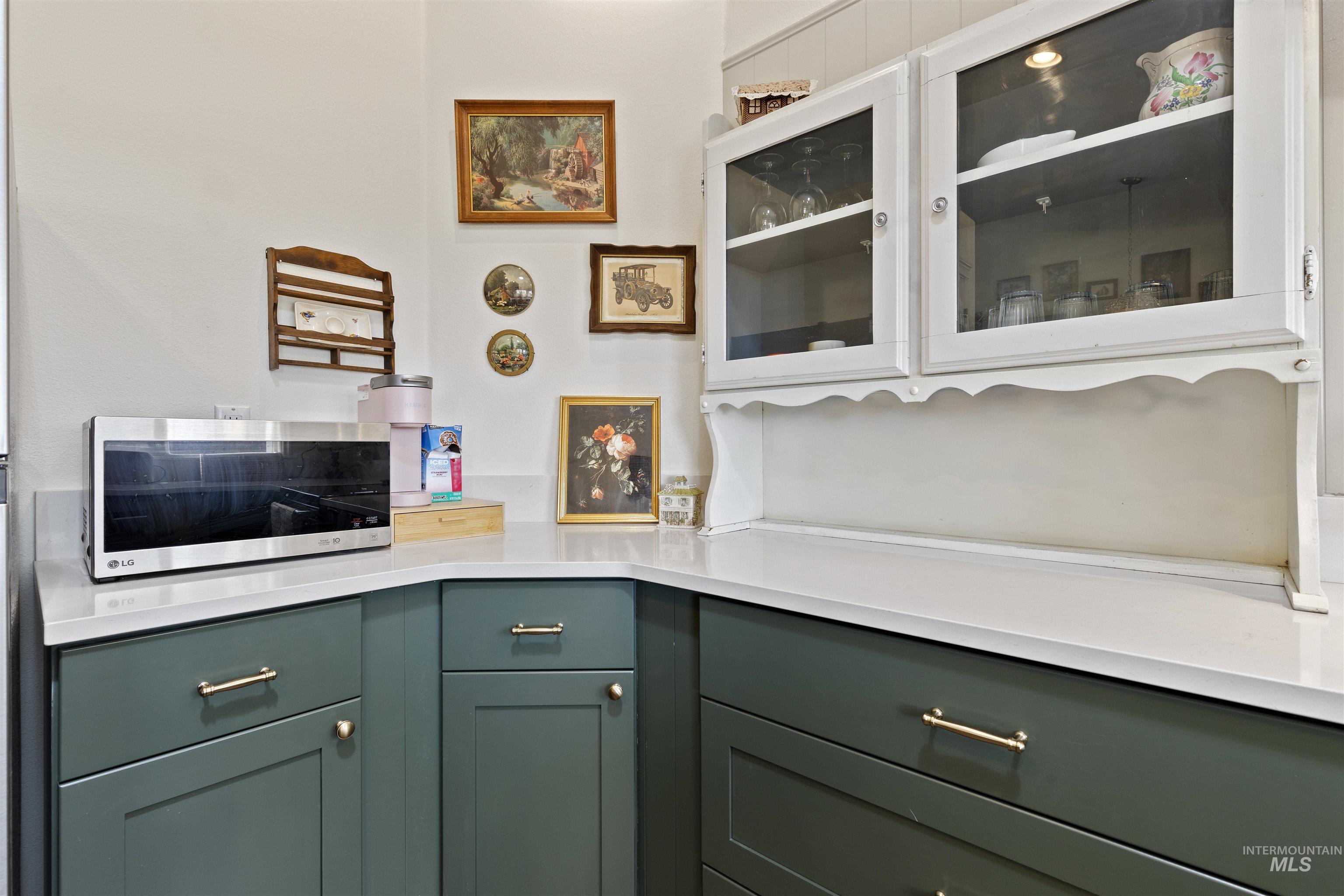 Kitchen with green cabinets, stainless steel microwave, glass insert cabinets, white cabinets, and light stone countertops