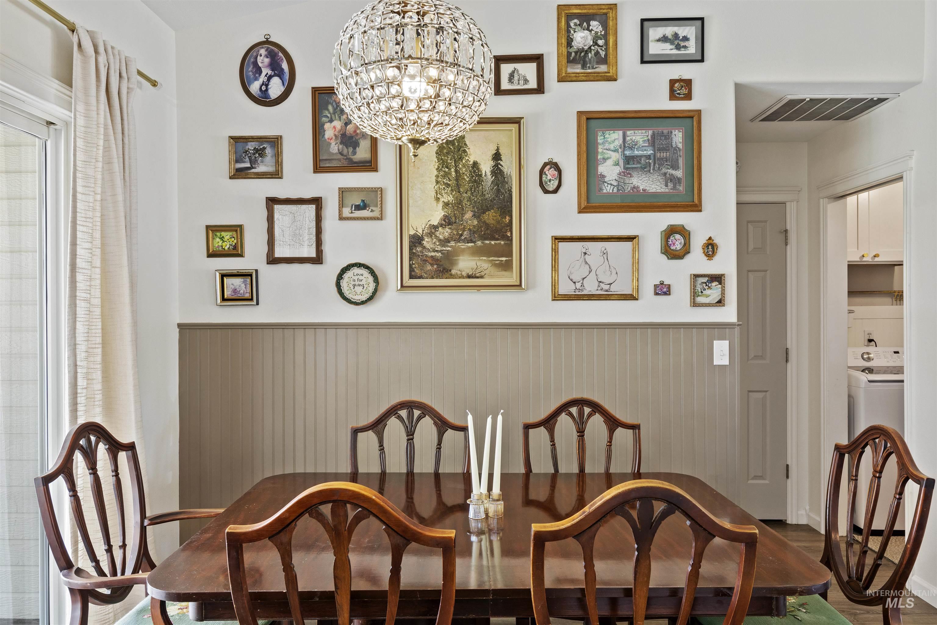 Dining area with a chandelier, washer / dryer, a wainscoted wall, and dark wood-style floors