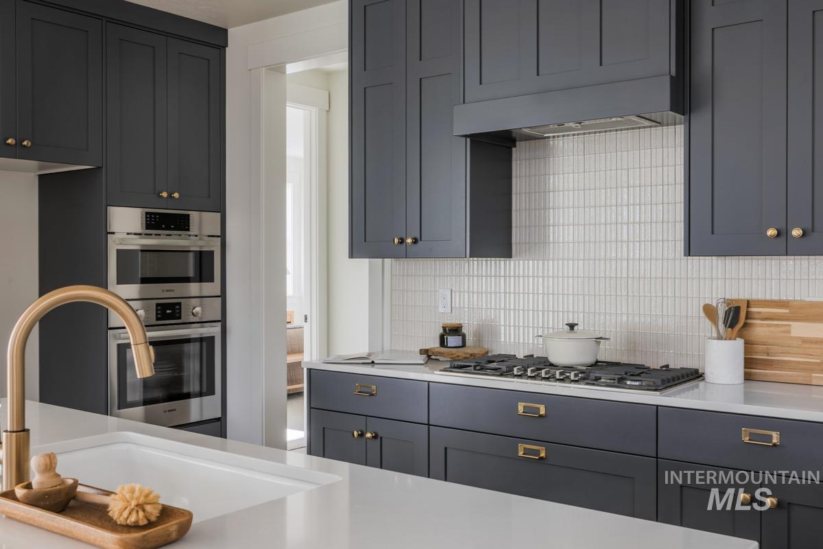 Kitchen featuring decorative backsplash, stainless steel appliances, light stone countertops, and gray cabinetry