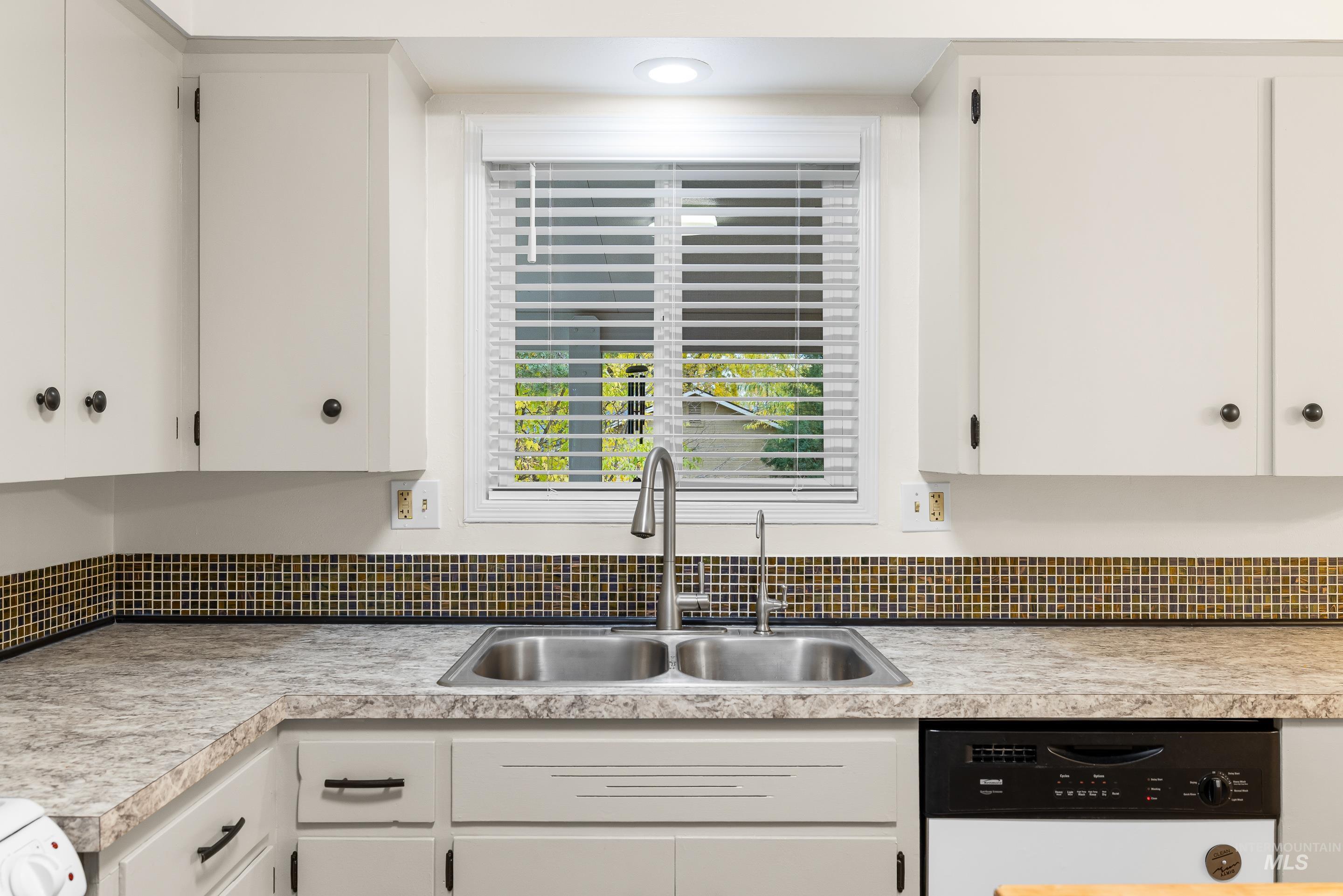 Kitchen with white cabinetry, white dishwasher, and light countertops