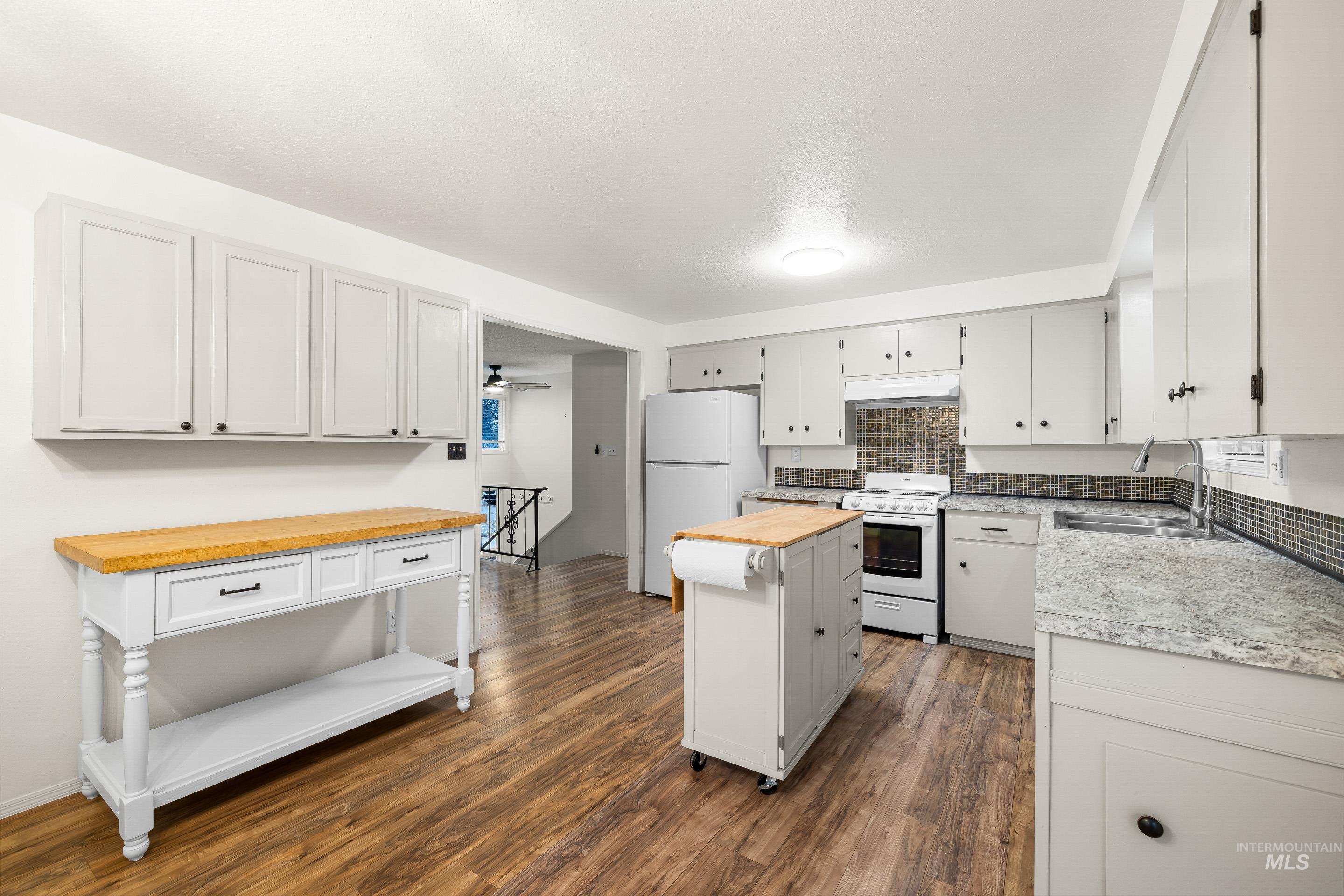 Kitchen with white appliances, dark wood-style flooring, butcher block countertops, tasteful backsplash, and white cabinets