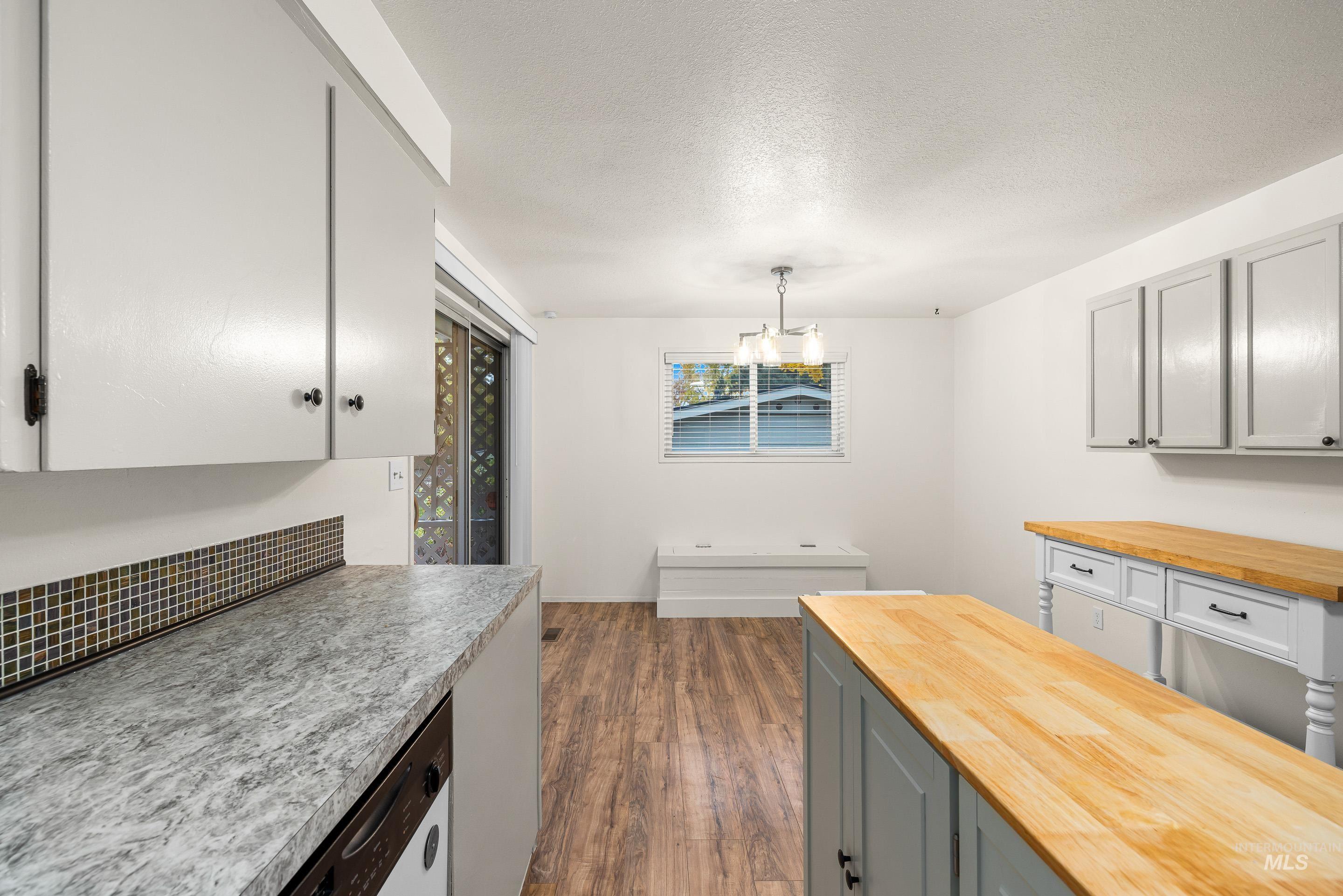 Kitchen with gray cabinetry, decorative light fixtures, dark wood-style floors, a textured ceiling, and stainless steel dishwasher