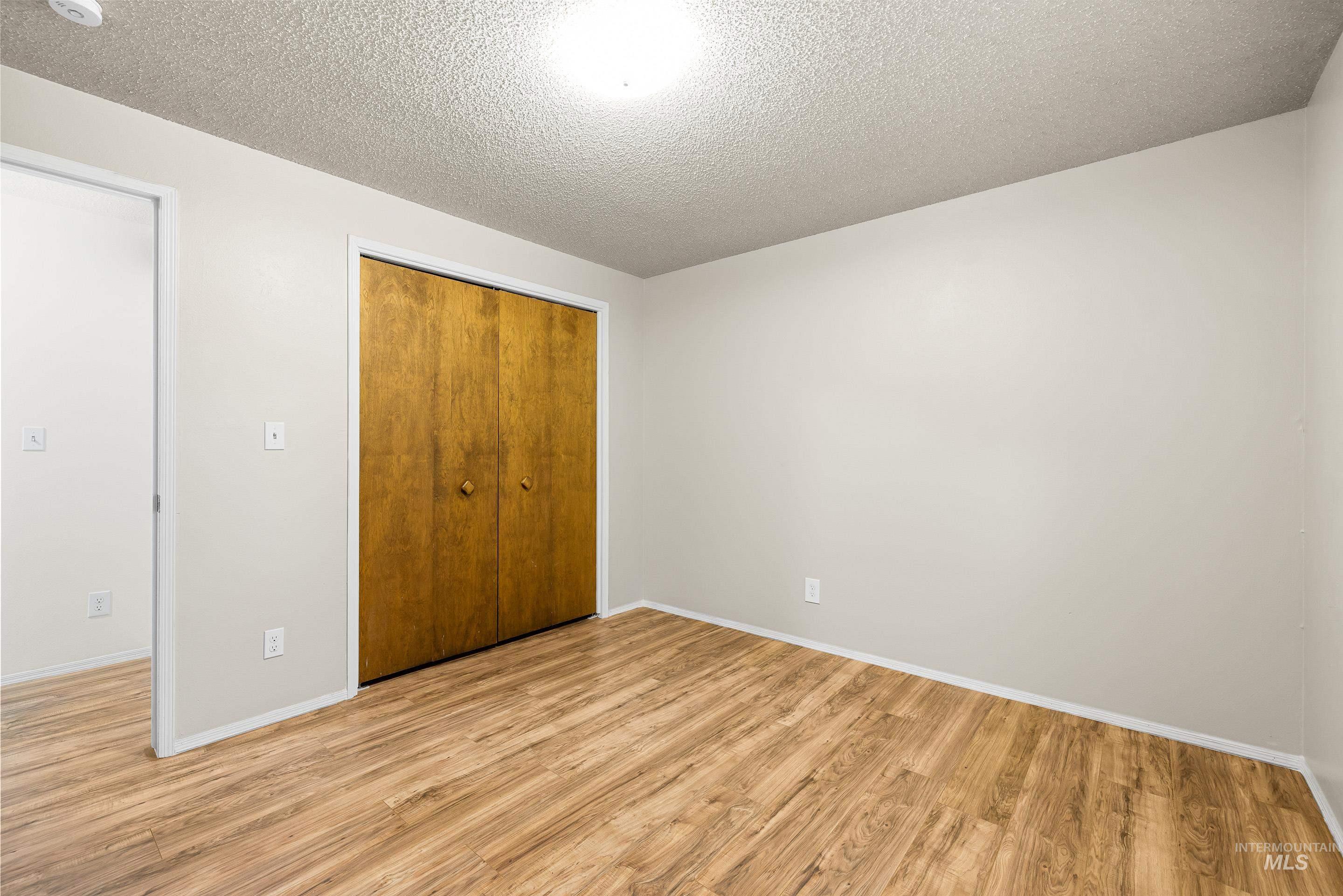 Unfurnished bedroom with a textured ceiling, light wood-style flooring, and a closet