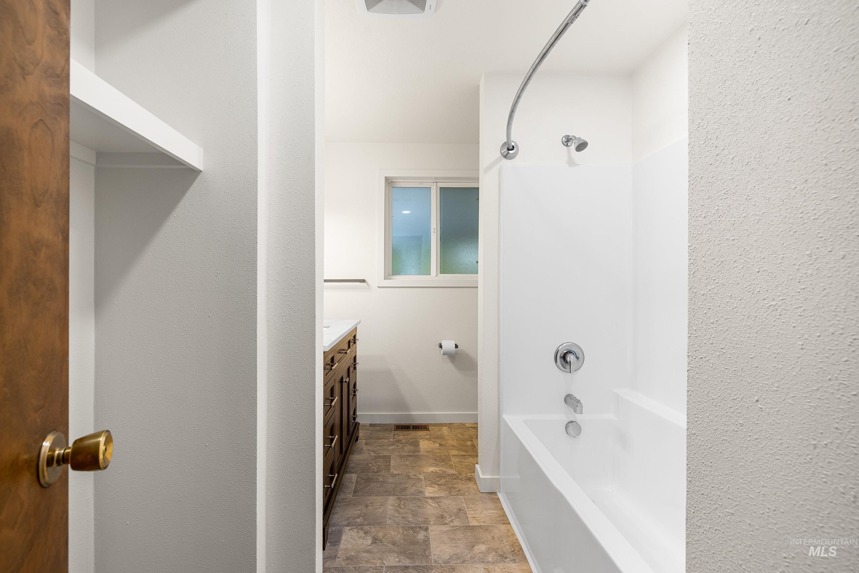 Full bath featuring vanity, washtub / shower combination, and stone finish flooring