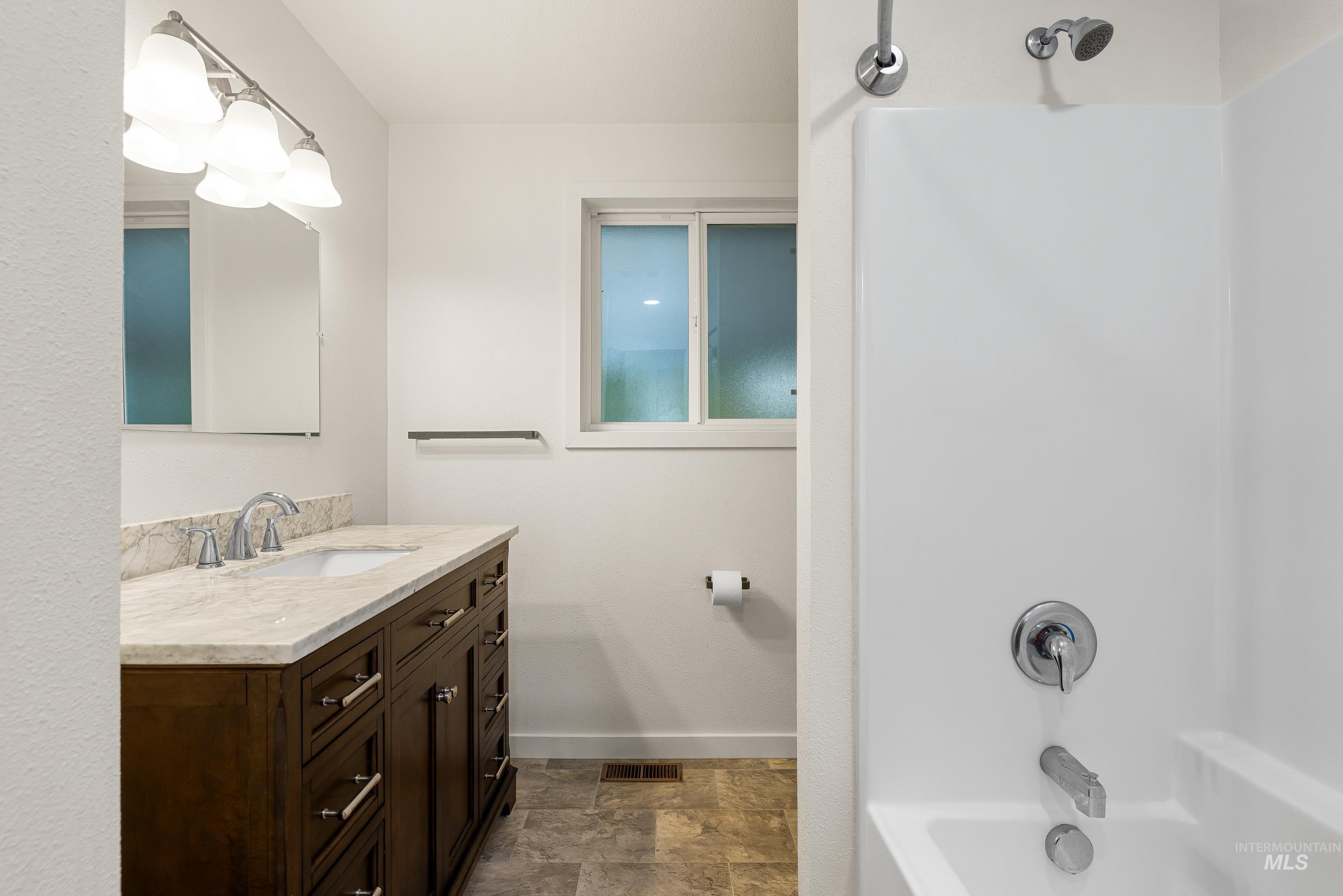 Bathroom featuring bathing tub / shower combination, vanity, and stone finish flooring