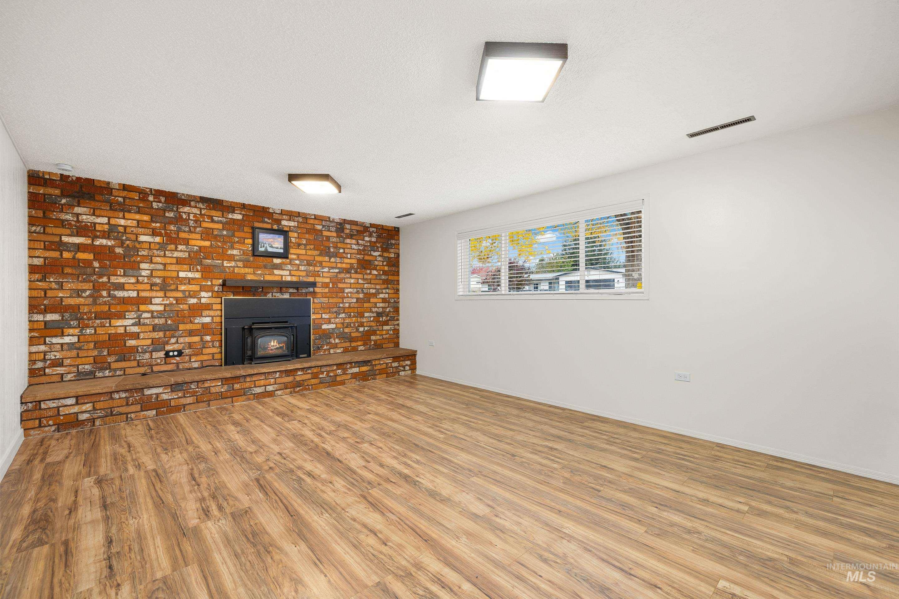Unfurnished living room featuring wood finished floors, brick wall, and a wood stove
