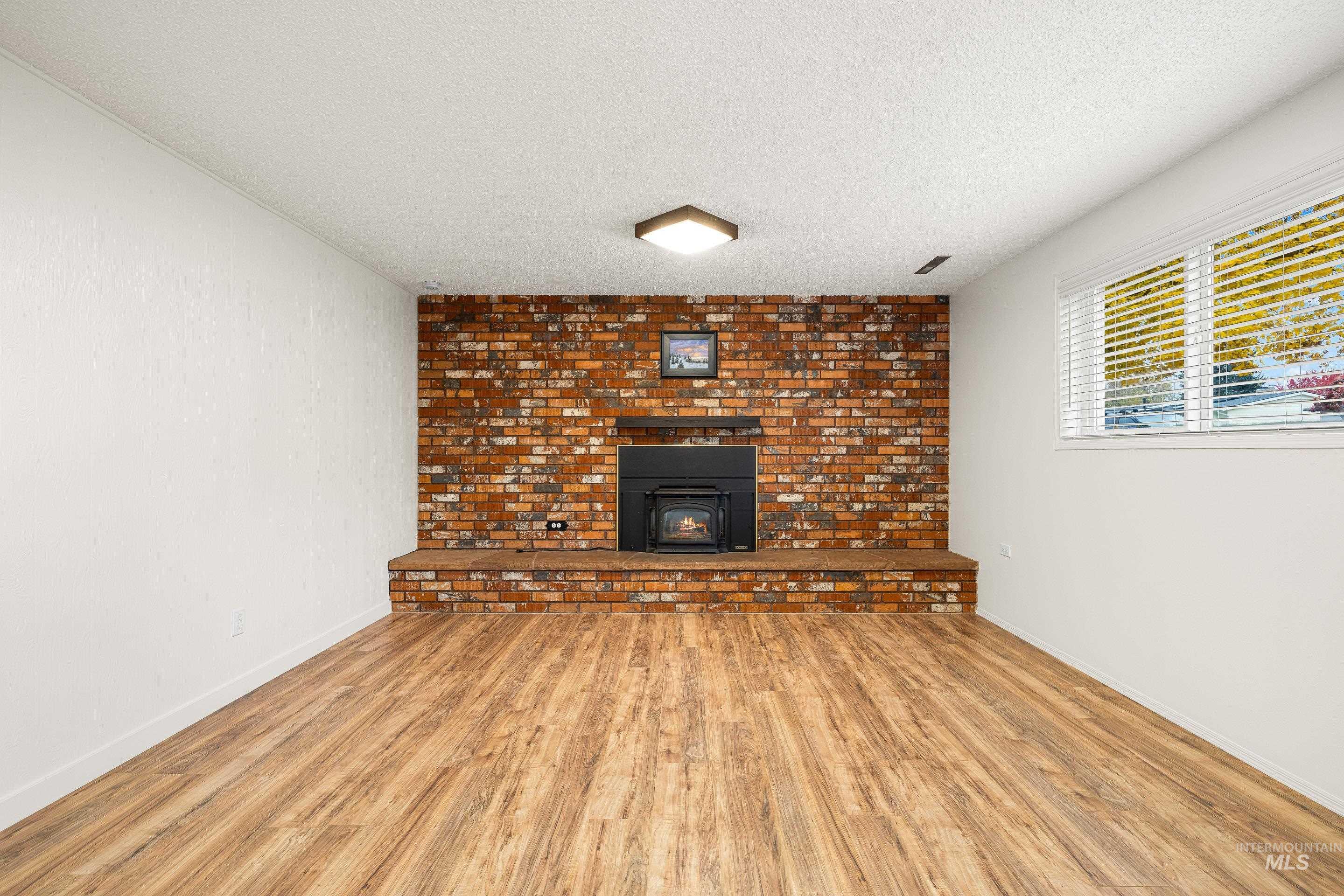 Unfurnished living room featuring a textured ceiling, wood finished floors, and a wood stove