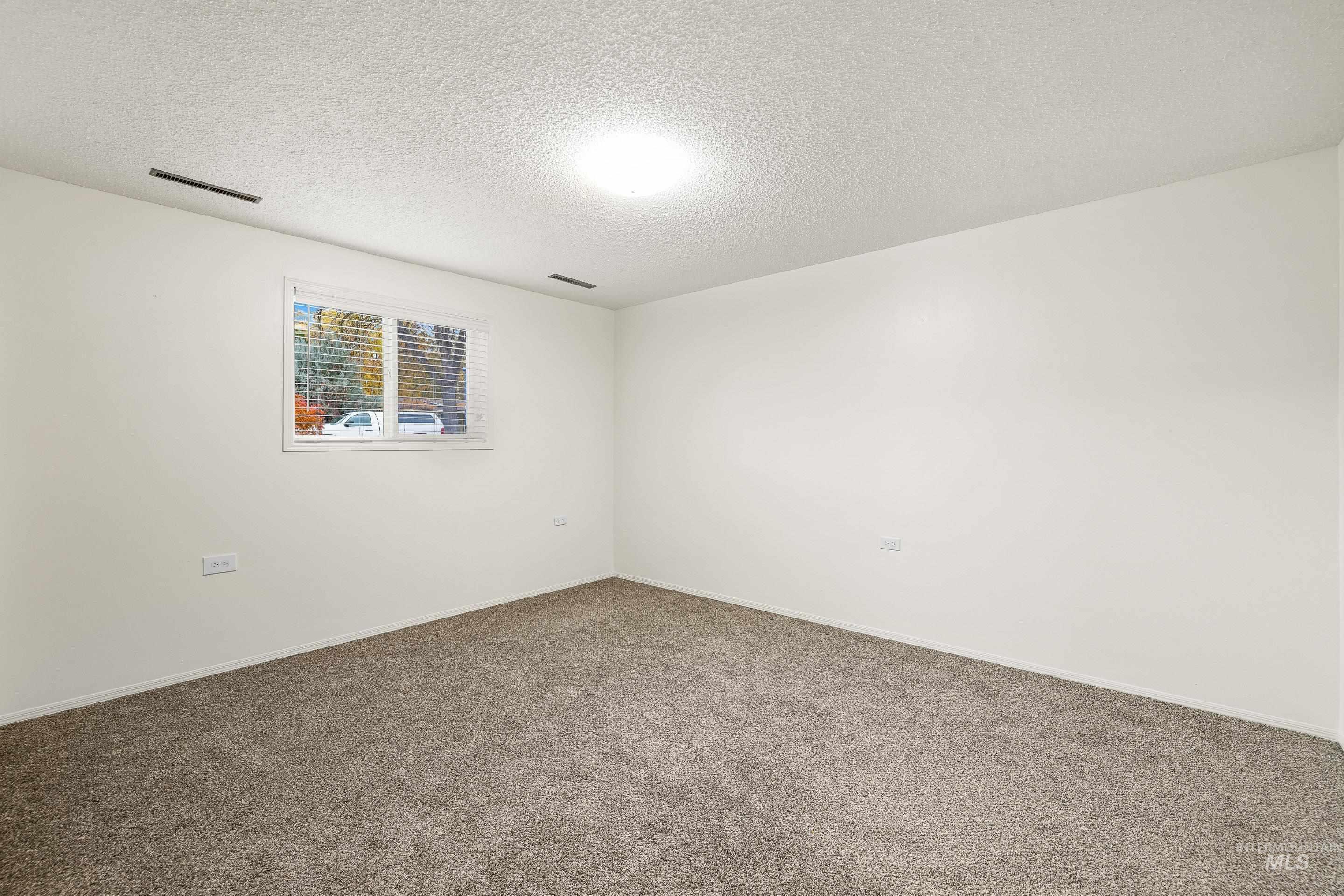Carpeted empty room with a textured ceiling and baseboards