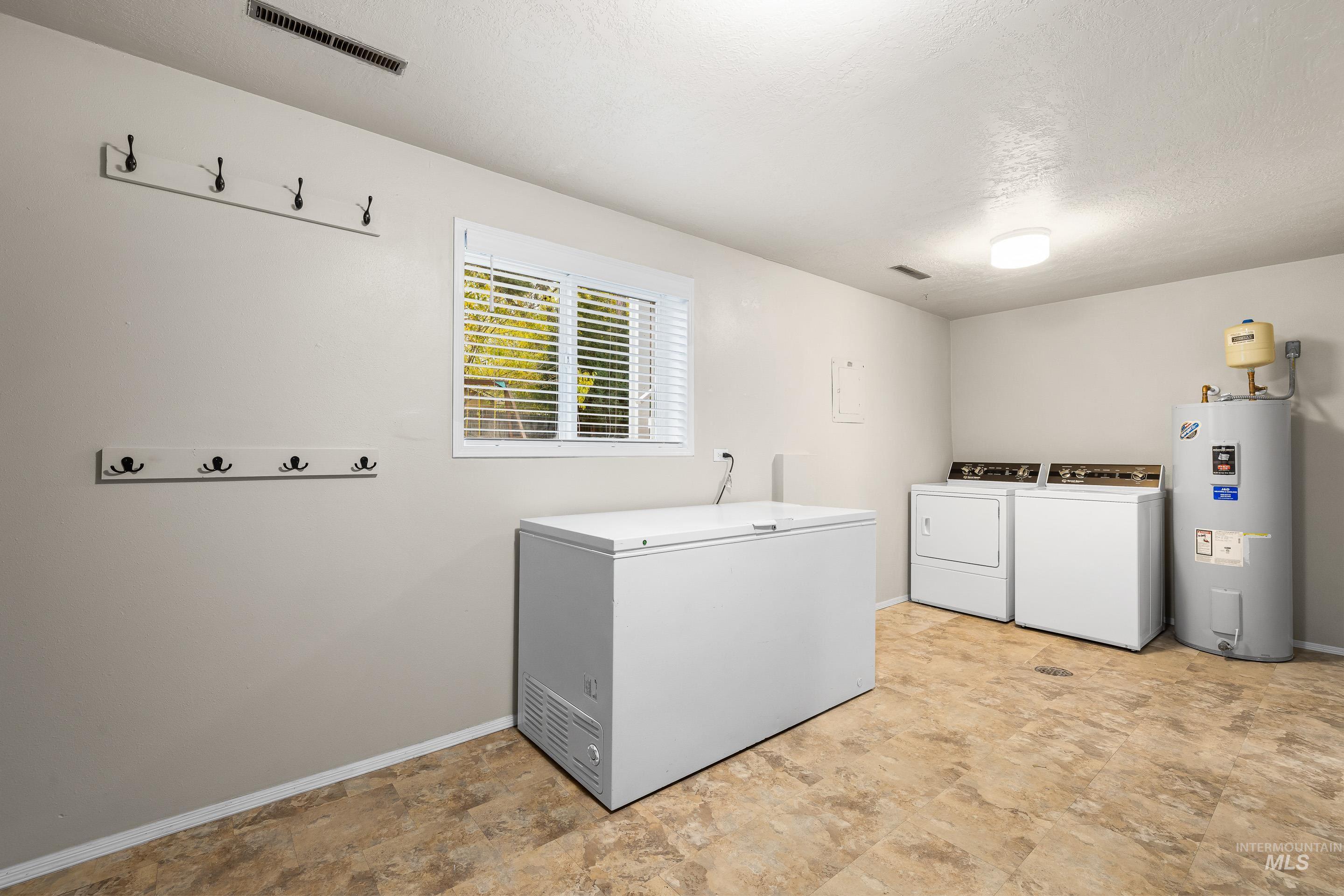 Washroom with water heater, stone finish flooring, washing machine and clothes dryer, and a textured ceiling