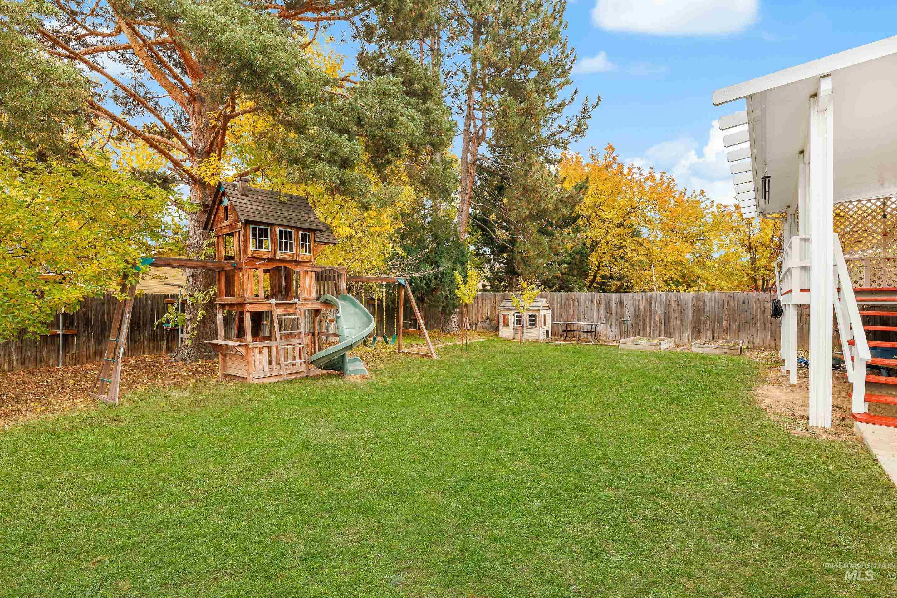 Fenced backyard with a playground and view of scattered trees