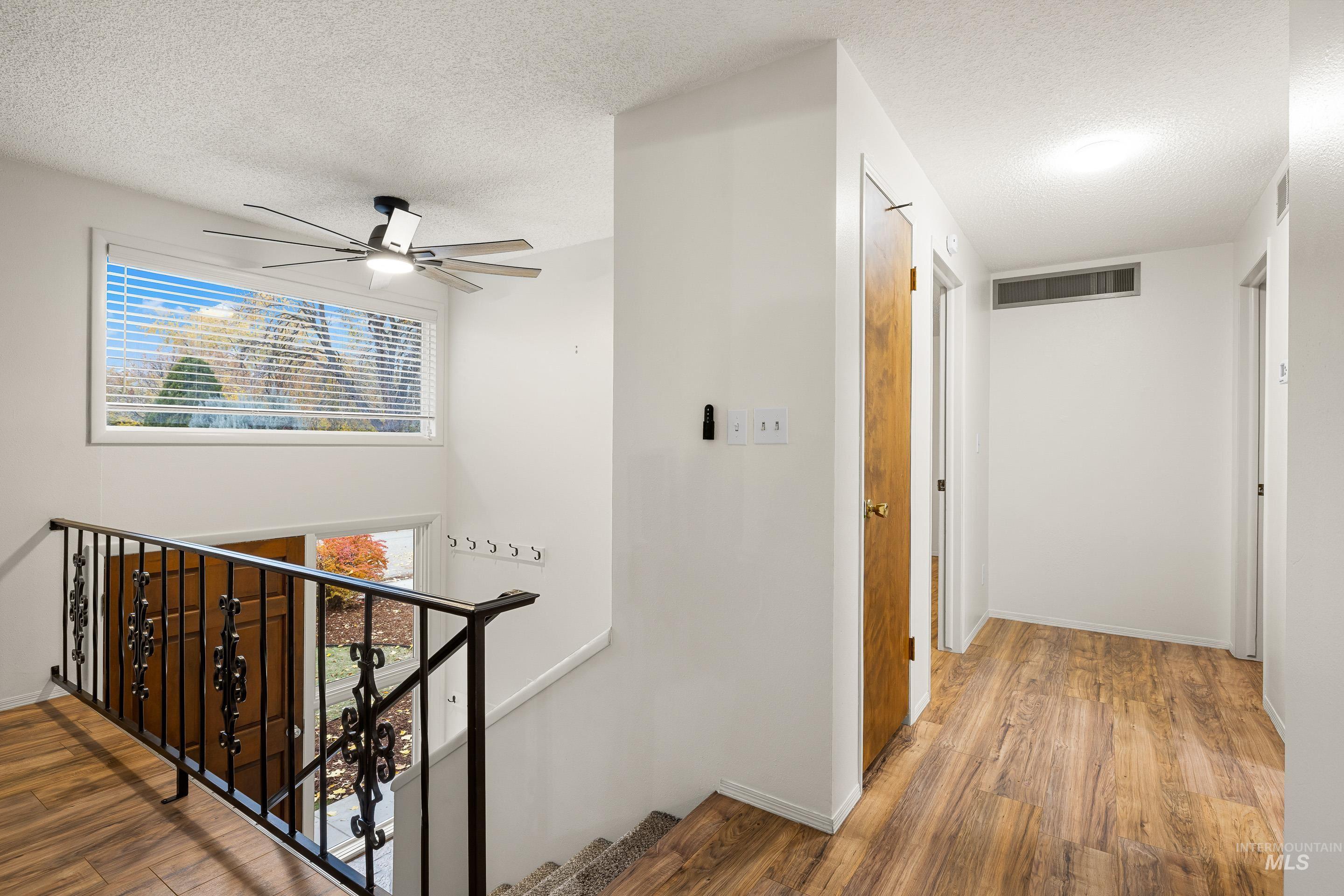 Corridor featuring healthy amount of natural light, wood finished floors, a textured ceiling, and an upstairs landing