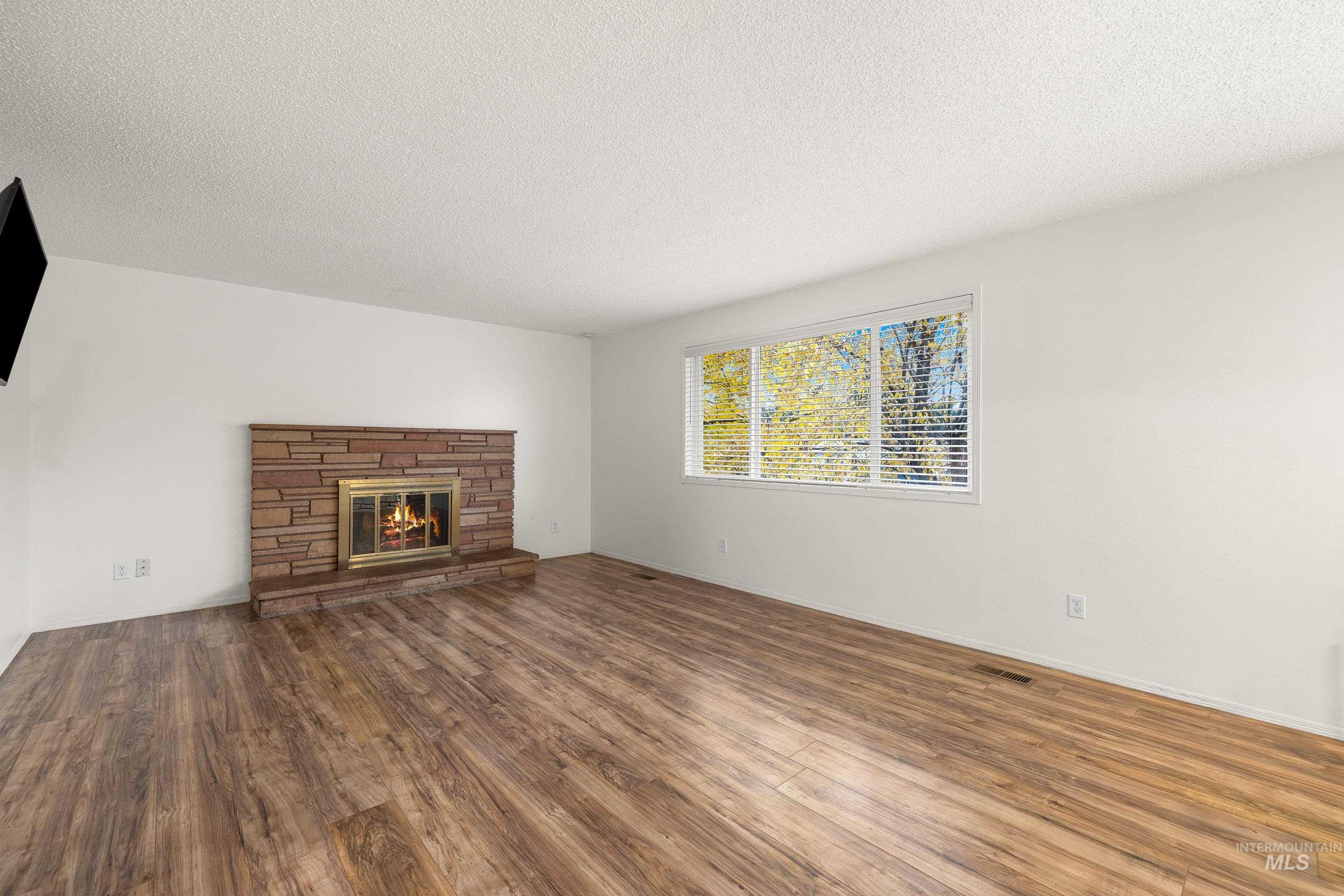 Unfurnished living room featuring a textured ceiling, a stone fireplace, and wood finished floors