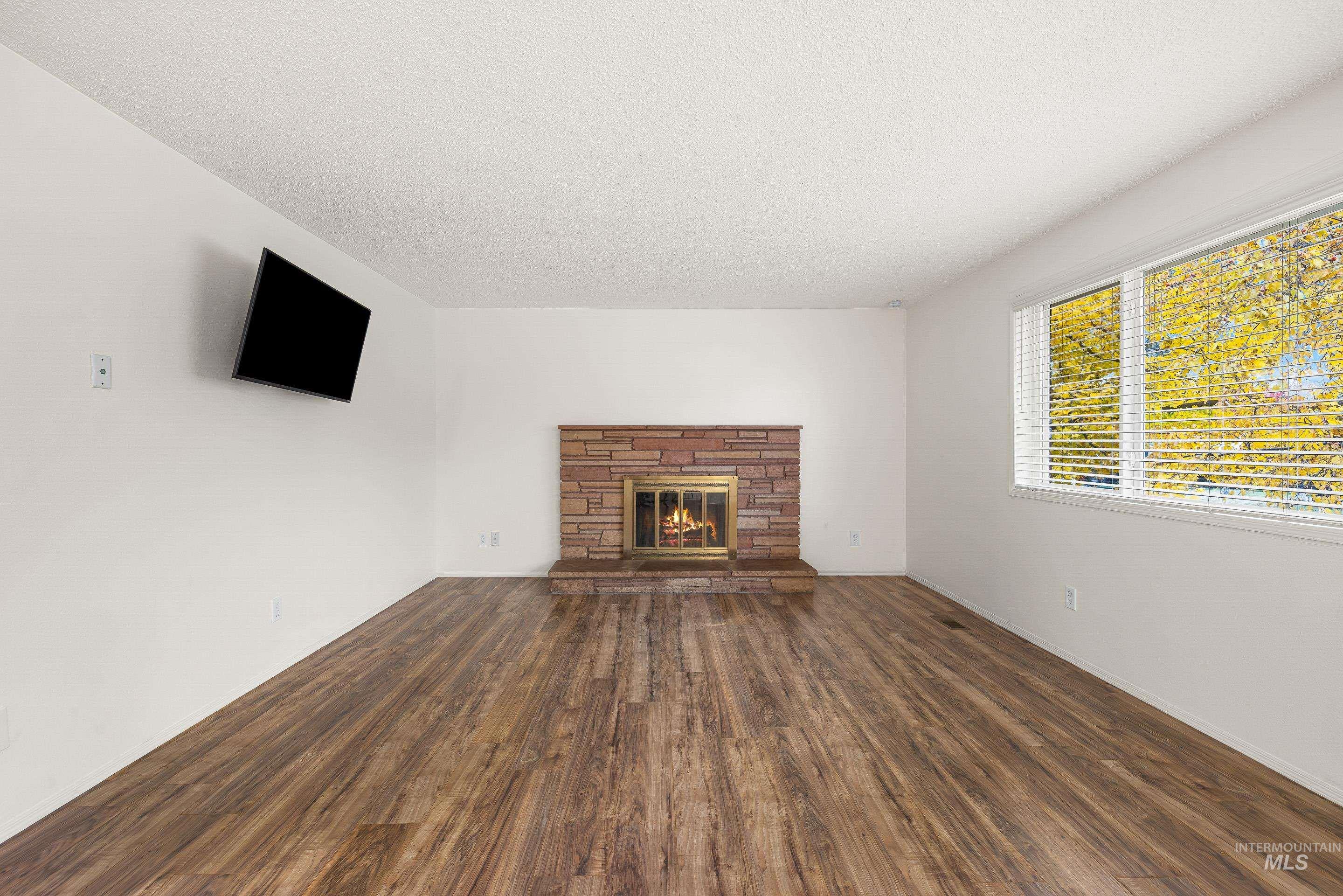 Unfurnished living room with a fireplace, dark wood-style floors, and a textured ceiling