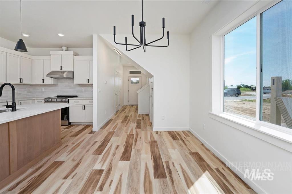 Kitchen featuring white cabinetry, a chandelier, tasteful backsplash, stainless steel range oven, and light wood finished floors