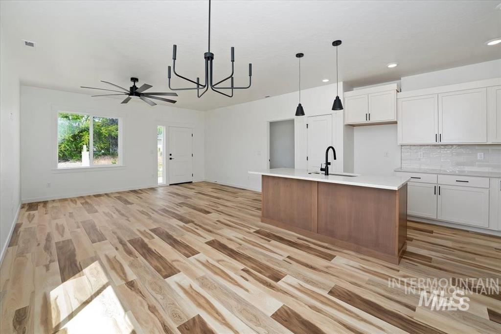 Kitchen with white cabinetry, pendant lighting, a chandelier, tasteful backsplash, and brown cabinets