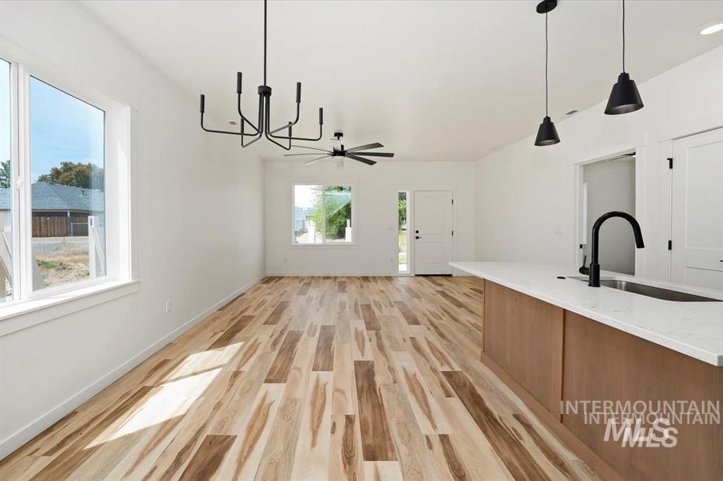 Kitchen featuring pendant lighting, light wood finished floors, a chandelier, light stone counters, and brown cabinets