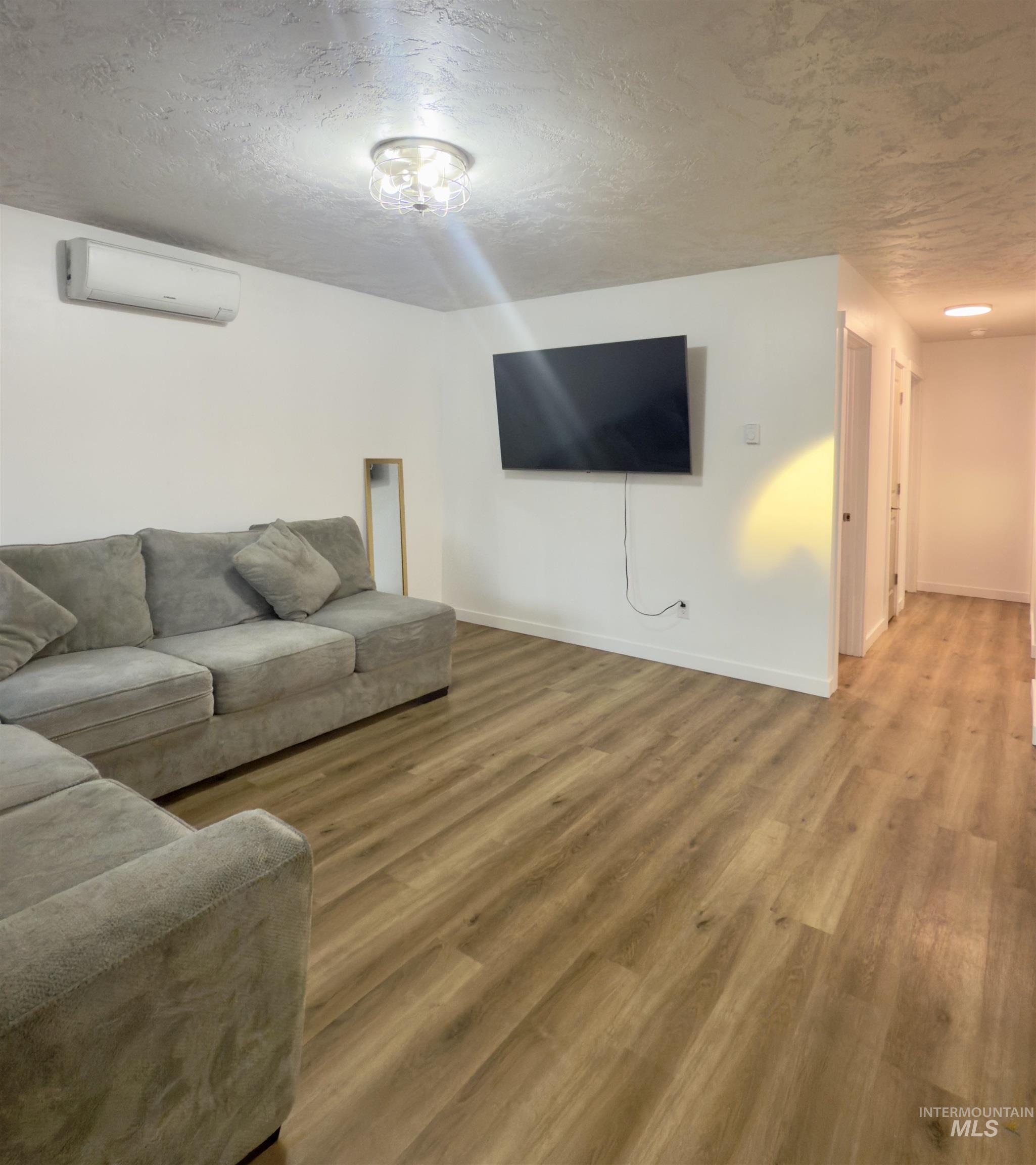 Living room featuring a textured ceiling, light wood-style floors, and an AC wall unit