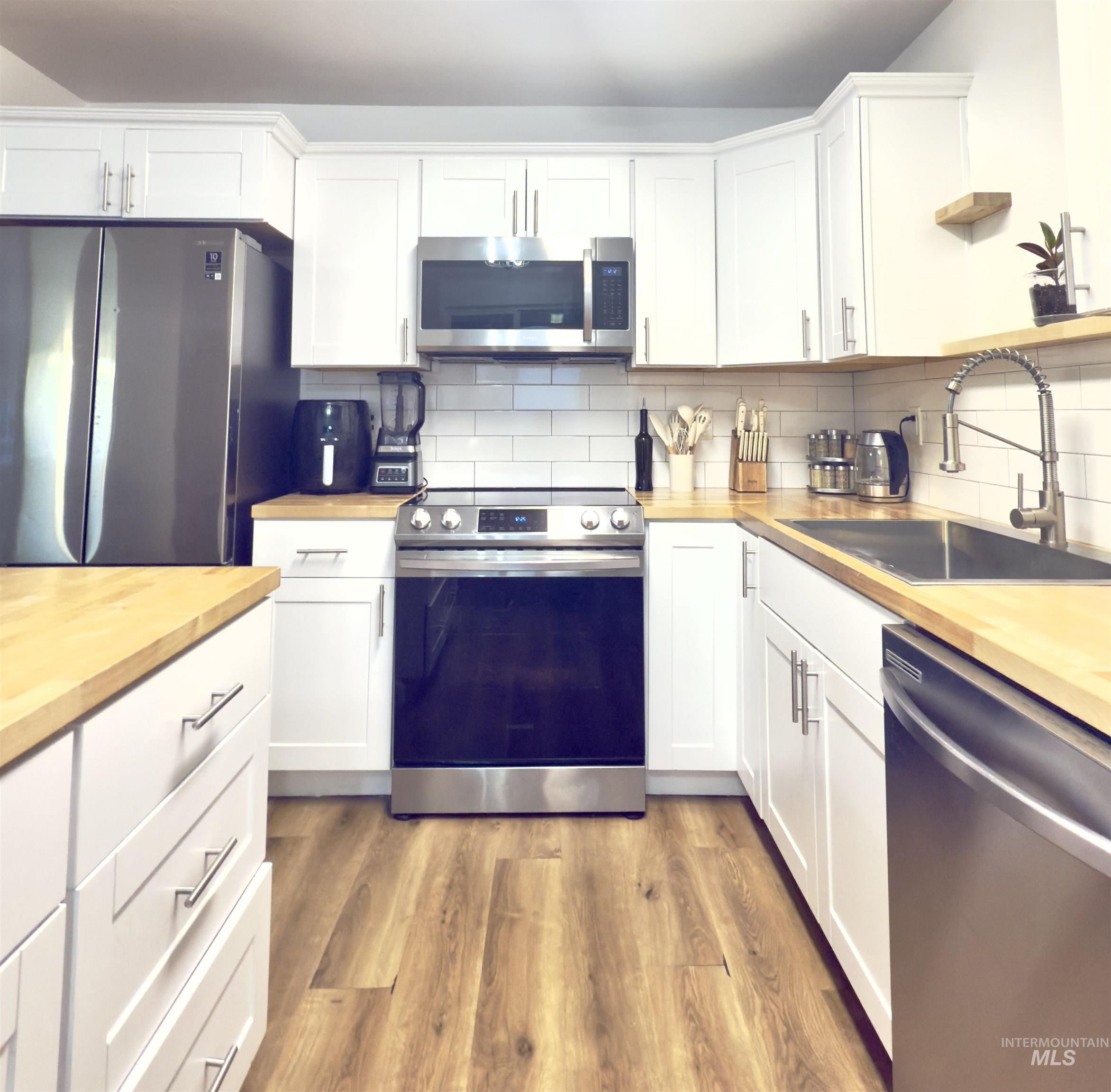 Kitchen with appliances with stainless steel finishes, white cabinetry, butcher block countertops, and dark wood-type flooring
