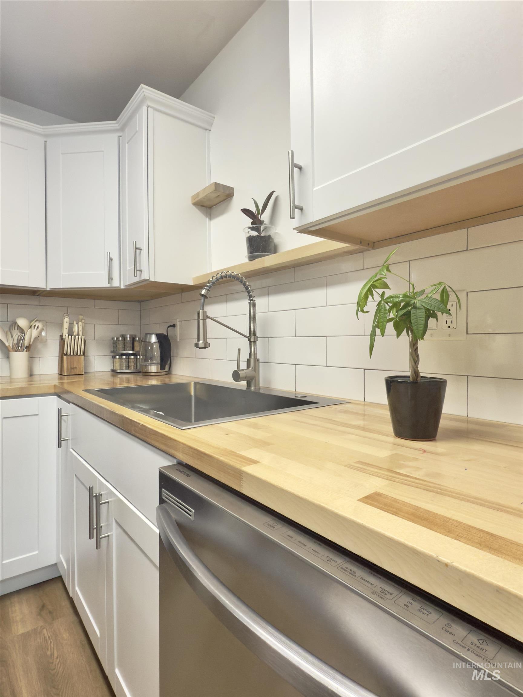 Kitchen with dishwasher, white cabinets, butcher block countertops, decorative backsplash, and dark wood-style floors