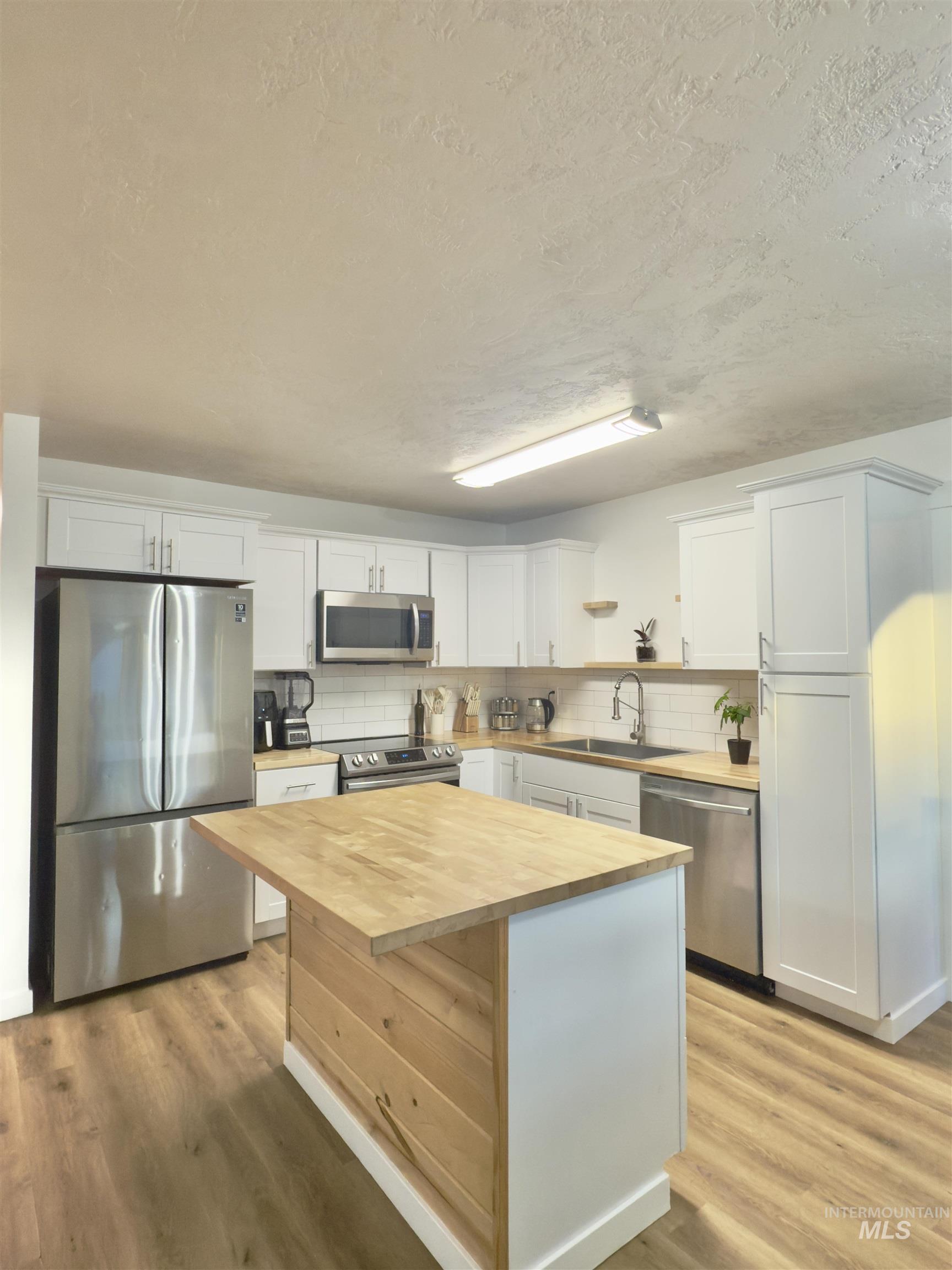 Kitchen featuring appliances with stainless steel finishes, white cabinets, wooden counters, a center island, and a textured ceiling